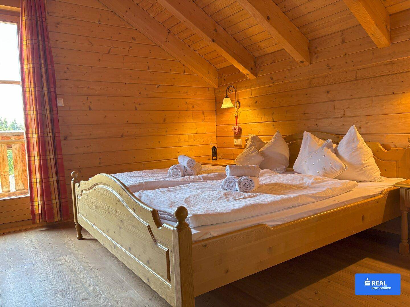 Helles Schlafzimmer mit Doppelbett, Holzwänden, sichtbaren Deckenbalken und Zugang zum Balkon.