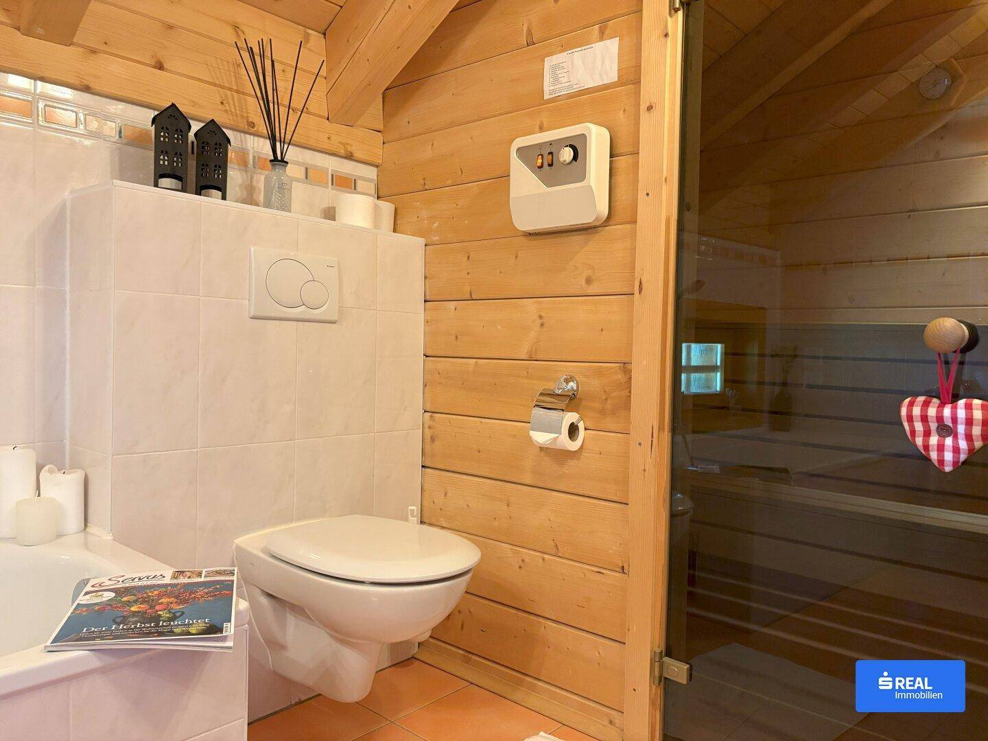 Badezimmer mit wandhängendem WC und einer integrierten Sauna, umgeben von Holzwänden und Fliesenboden.