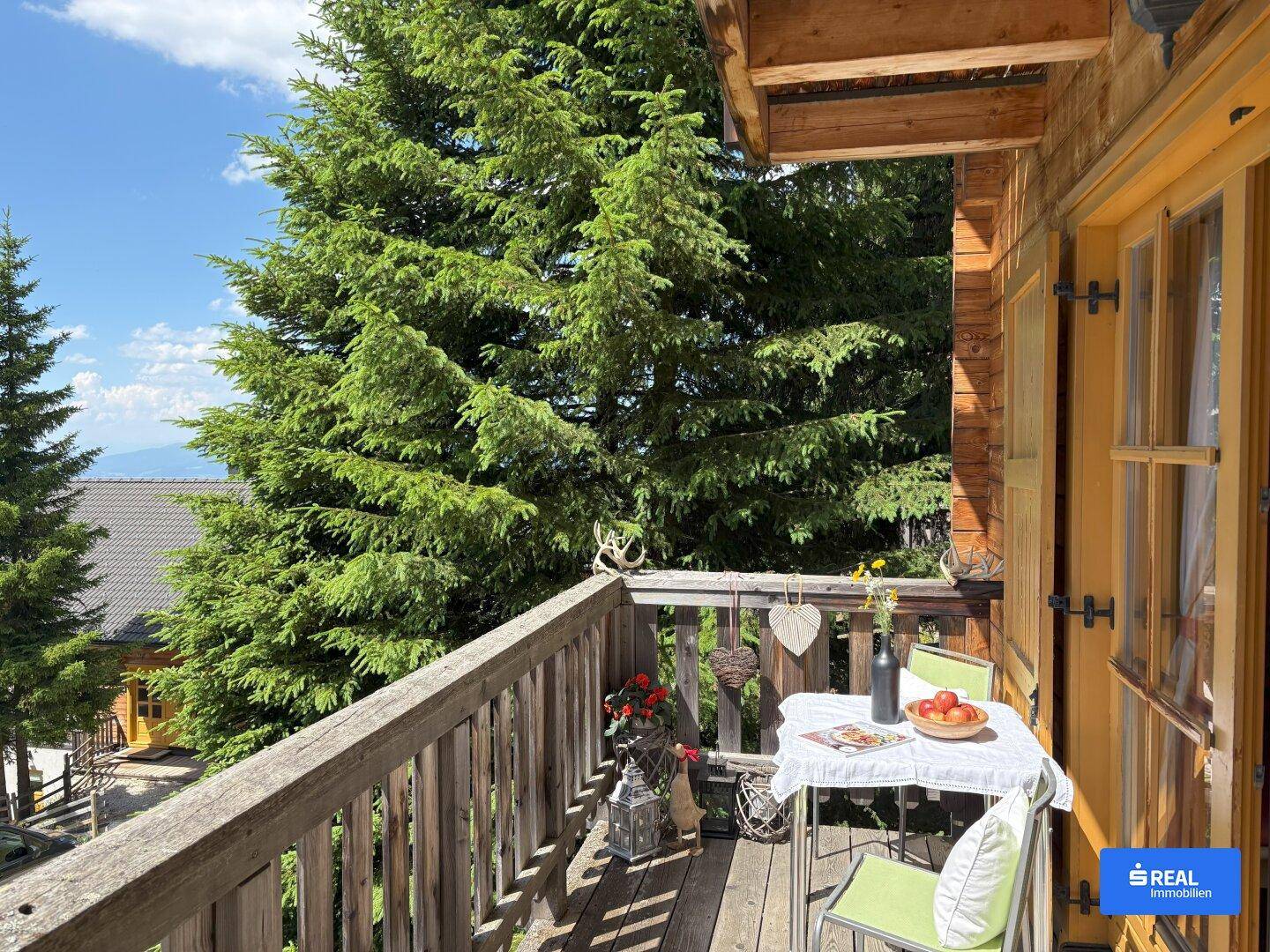 Gemütlicher Balkon mit Sitzgelegenheiten, umgeben von hohen Nadelbäumen und weitem Bergblick.