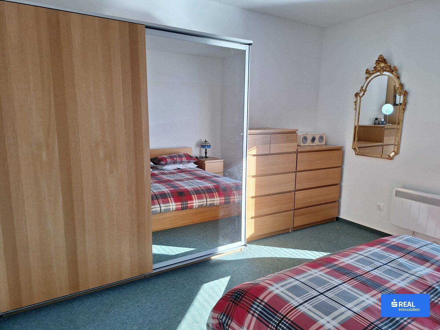 Schlafzimmer mit einem großen Spiegelschrank, Holzkommode und Teppichboden.