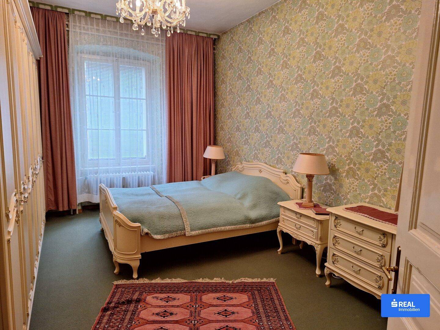 Schlafzimmer im traditionellen Stil mit floraler Tapete, klassischem Bett und passenden Nachttischen.