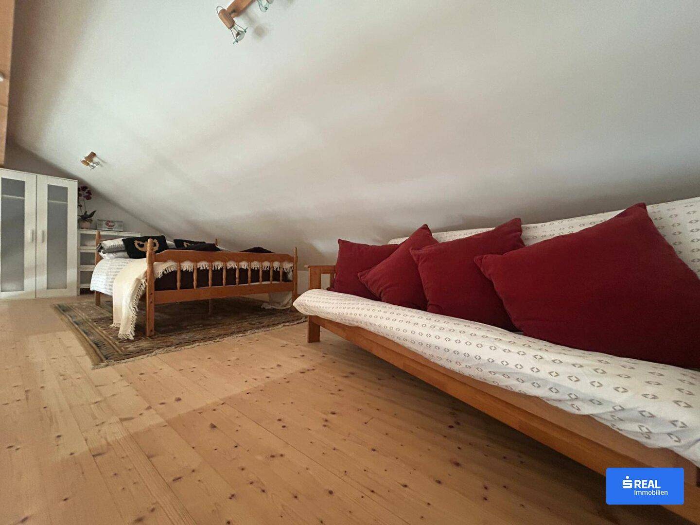 Gemütlicher Schlafbereich im Dachgeschoss mit Holzboden und einer Schlafcouch.