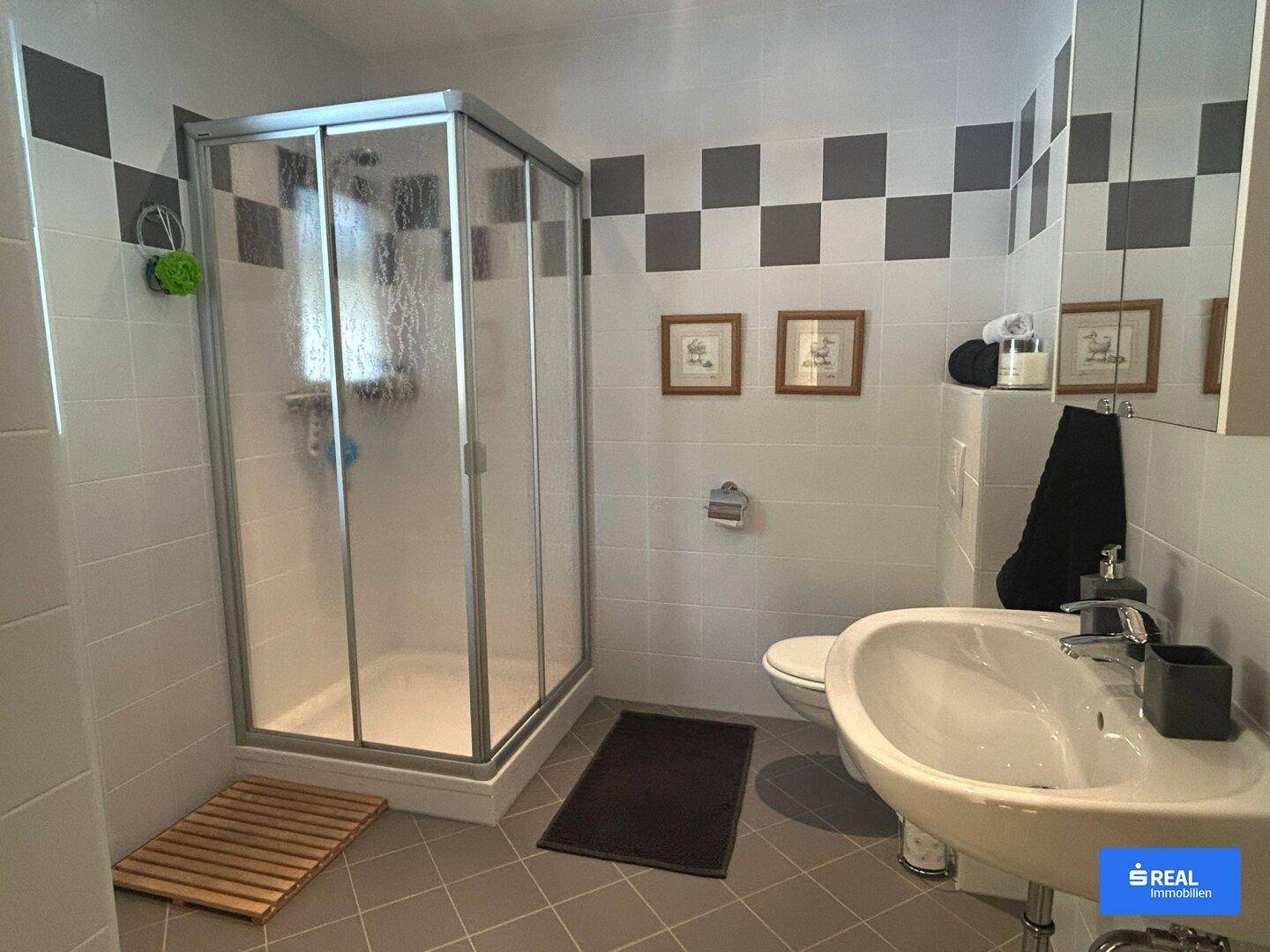 Badezimmer mit einer Duschkabine, Waschbecken und modernen Fliesen in Grau und Weiß.