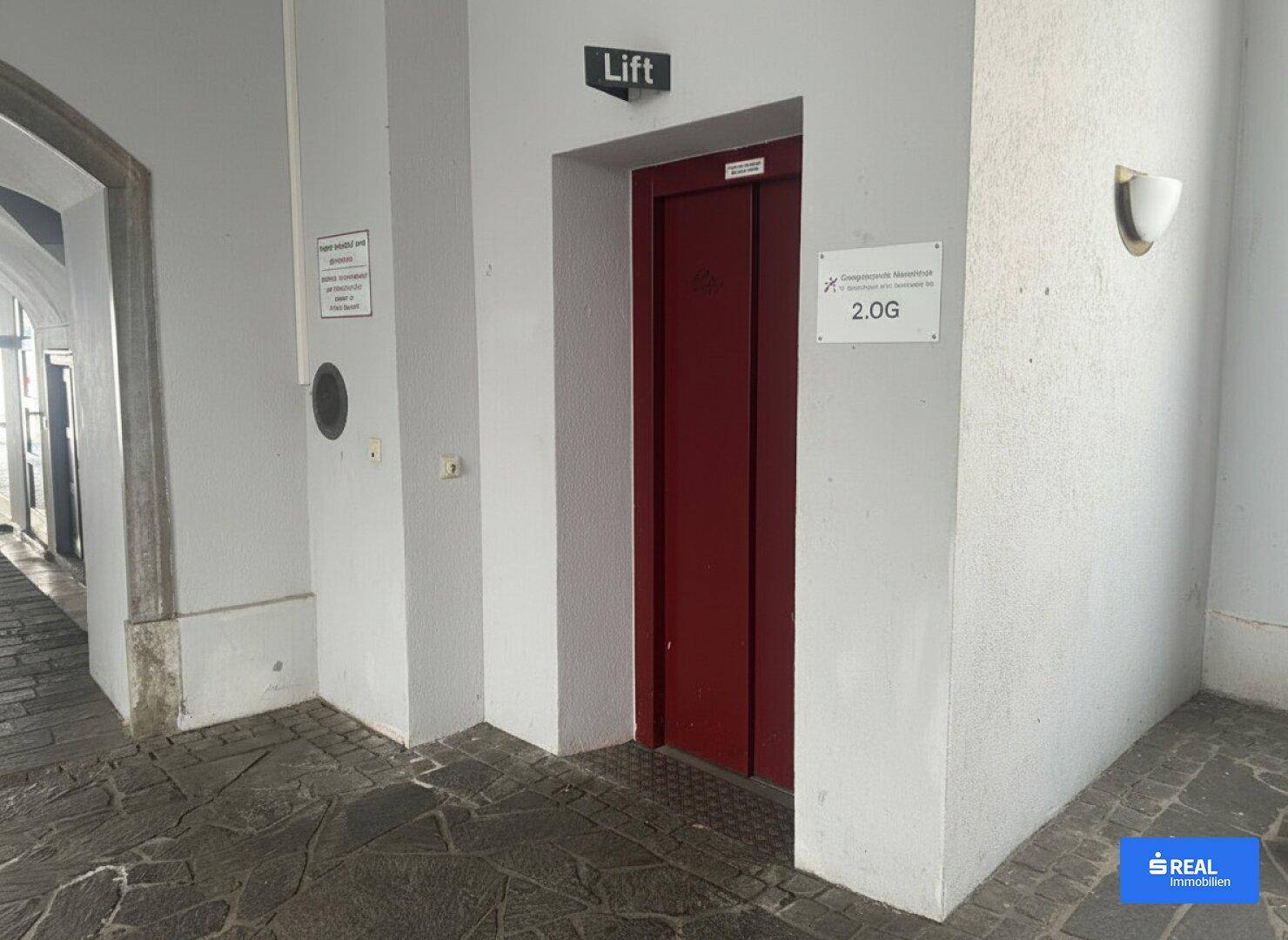 Innenansicht eines Flurs mit einer roten Aufzugtür und dem Schriftzug "Lift" darüber.