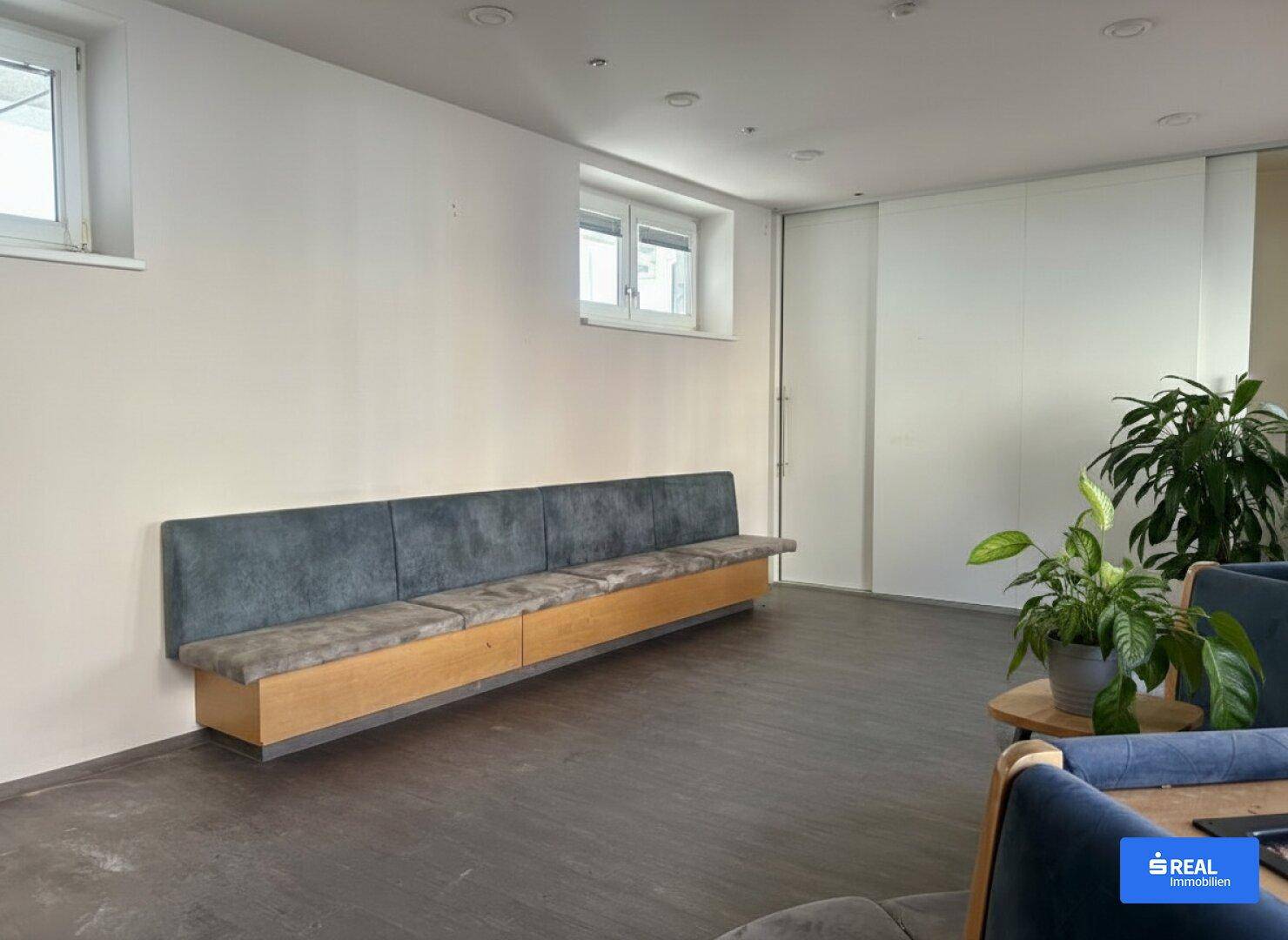 Langer, eingebauter Sitzbereich entlang einer weißen Wand mit kleinen Fenstern und Zimmerpflanzen.