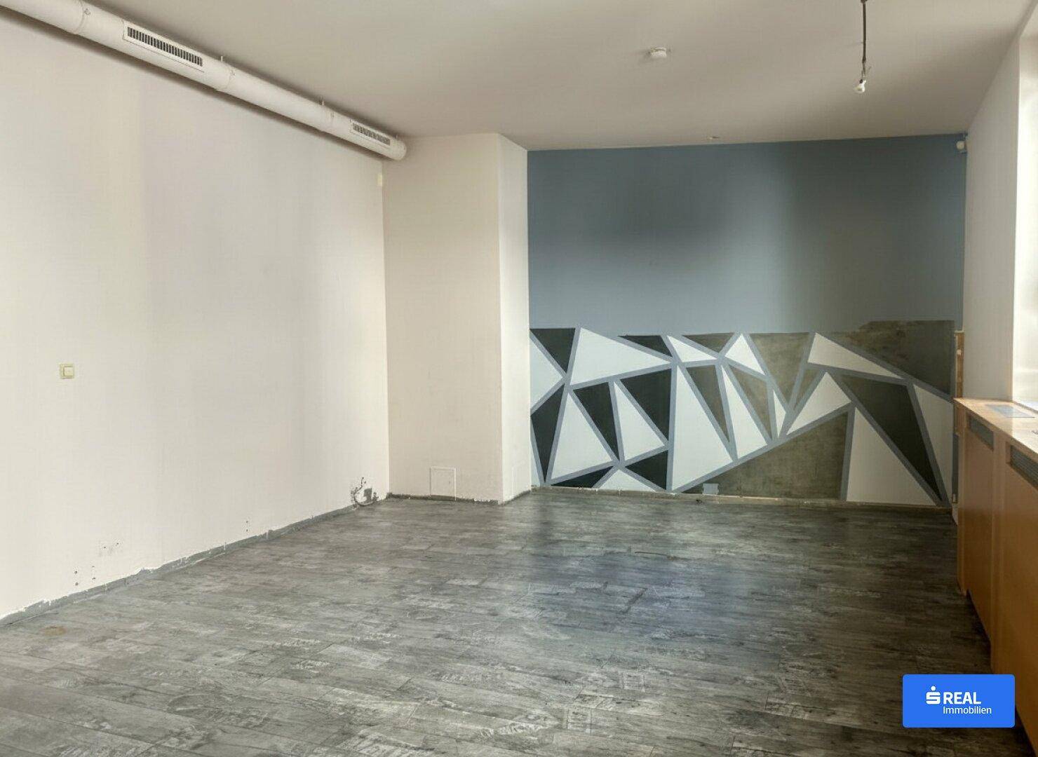 Leerer Innenraum mit einer auffälligen geometrischen Wandmalerei und dunklem Bodenbelag.