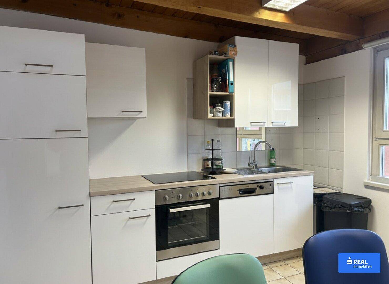 Moderne Einbauküche mit weißen Hochglanzfronten, Induktionskochfeld und Holzbalkendecke.
