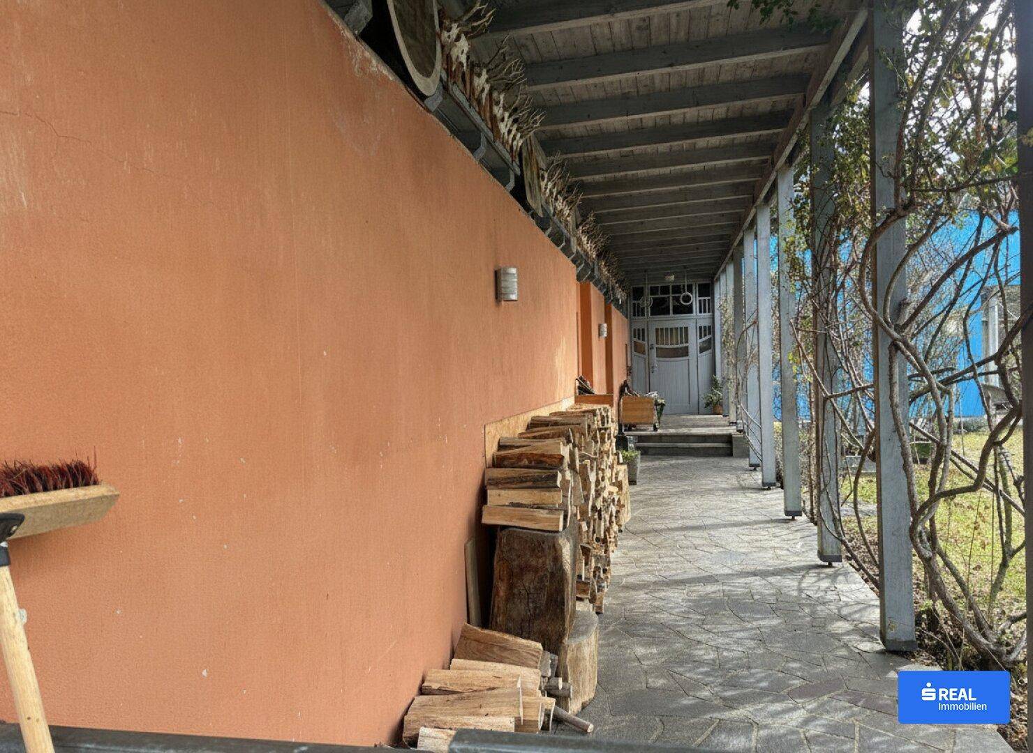 Überdachter Eingangsbereich mit Holzstapel und rustikalen Dekorationen an der orangefarbenen Wand.