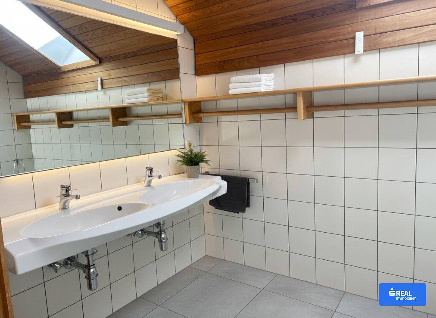 Modernes Badezimmer mit Doppelwaschbecken, großem Spiegel und Dachfenster für Tageslicht.