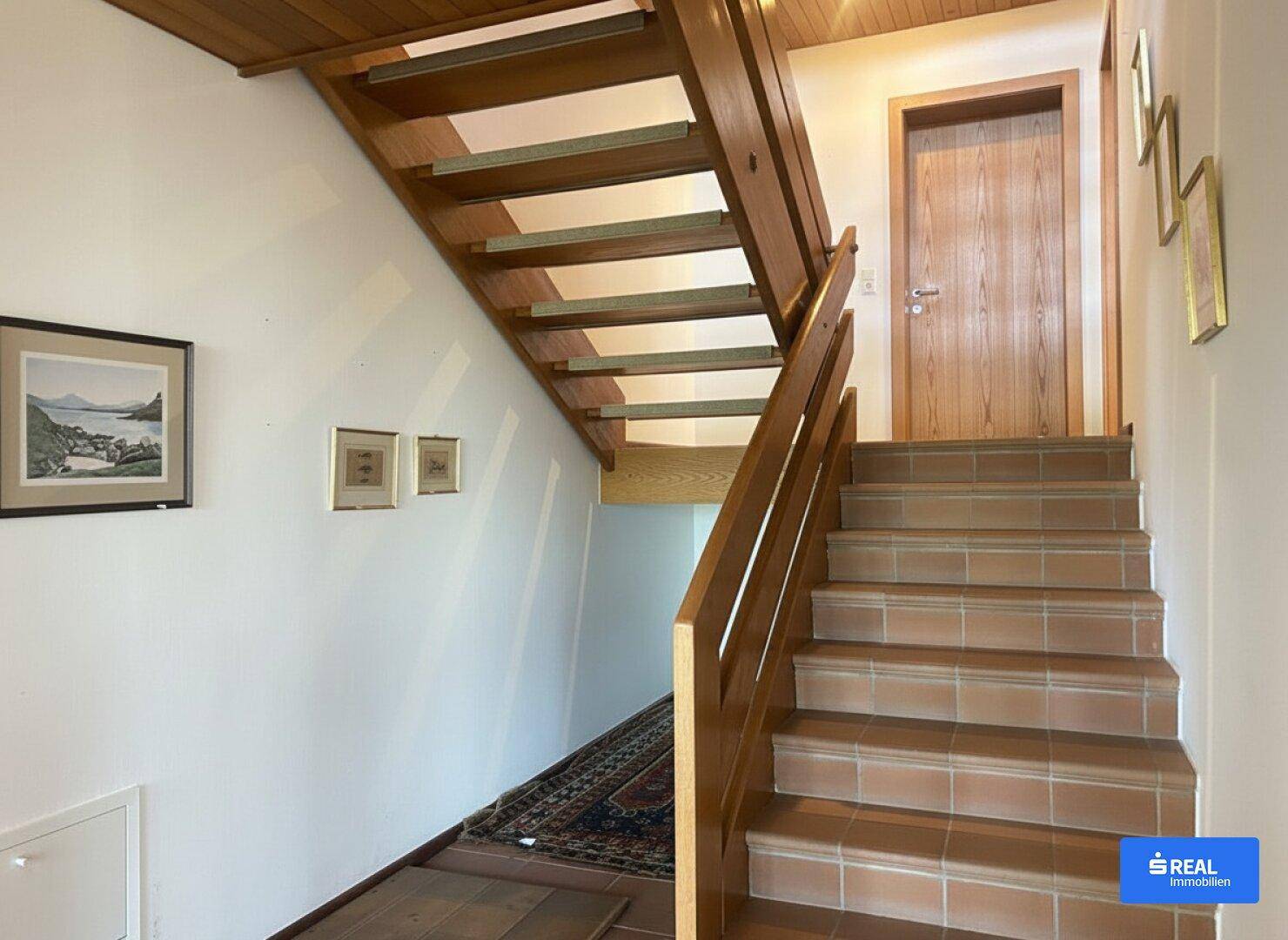 Heller Flur mit Holztreppe und Terrakottafliesen, der die verschiedenen Etagen verbindet.