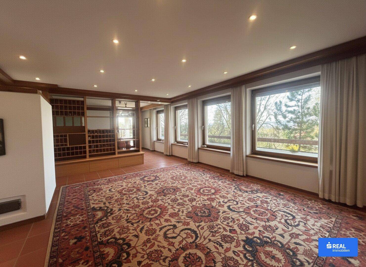 Geräumiges Wohnzimmer mit Terrakottafliesen, großem Teppich und vielen Fenstern mit Ausblick.