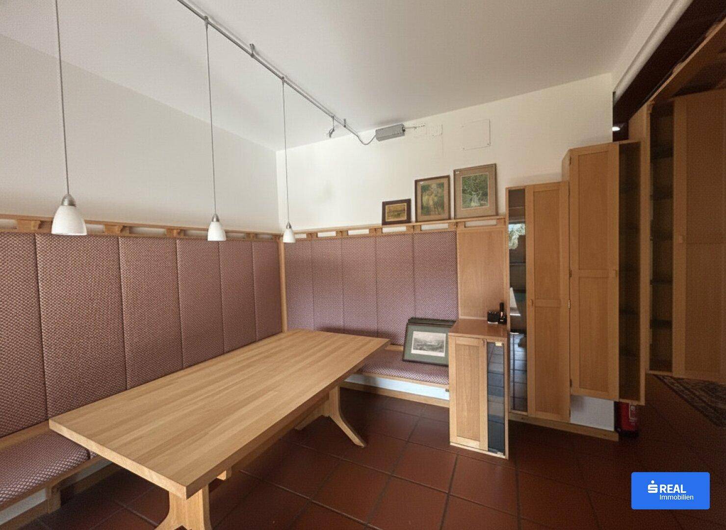 Gemütlicher Essbereich mit Holztisch, Sitzbänken und Terrakottafliesen am Boden.