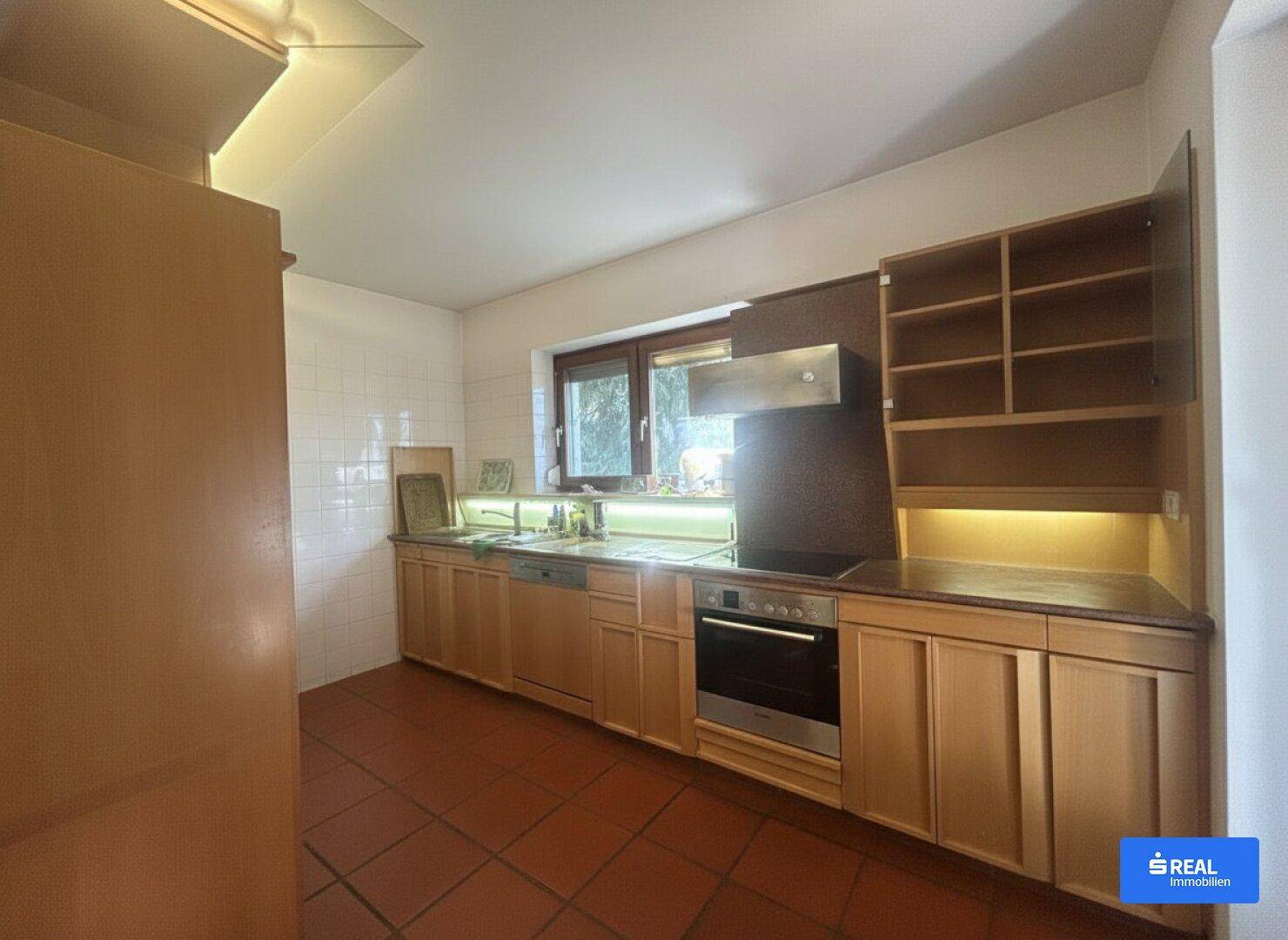 Funktionale Küche mit Holzfronten, Einbaugeräten und Terrakottafliesen am Boden.