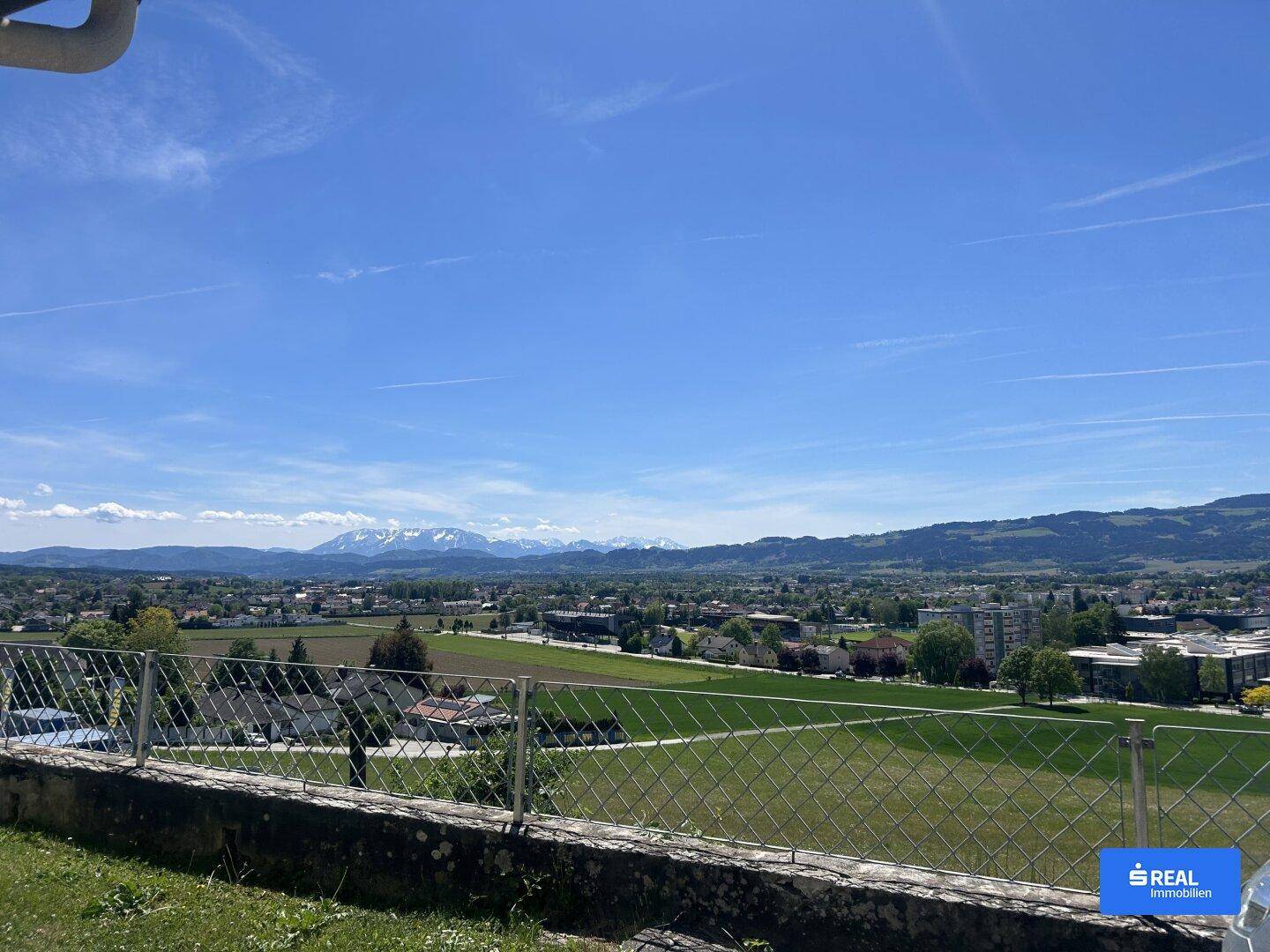 Weitläufiger Panoramablick über die Landschaft mit Bergen im Hintergrund unter einem klaren blauen Himmel.
