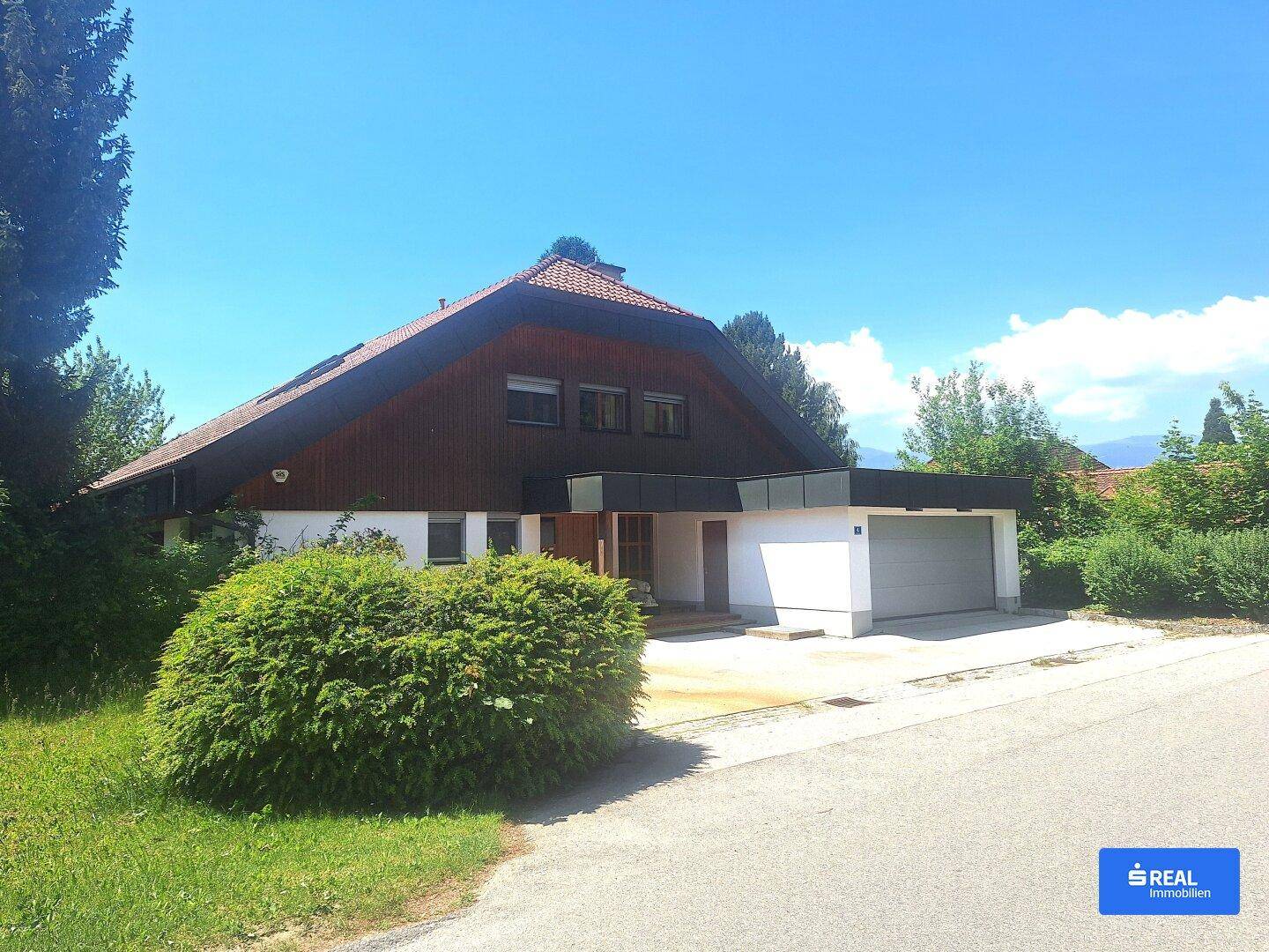 Vorderansicht des Hauses mit Doppelgarage und gepflegtem Vorgarten unter blauem Himmel.