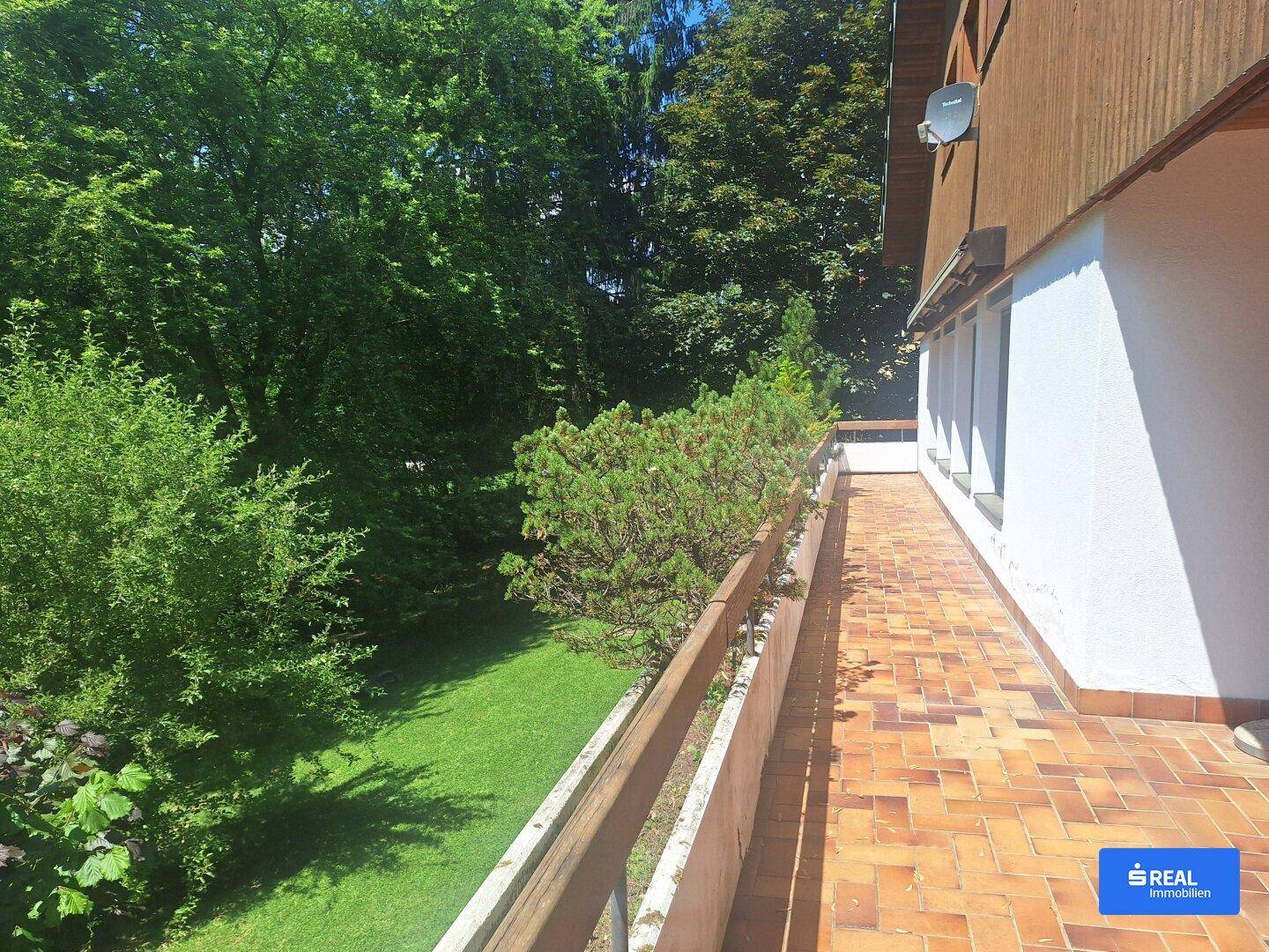 Lange, geflieste Terrasse mit Holzbalkonbrüstung und weitem Blick ins Grüne.
