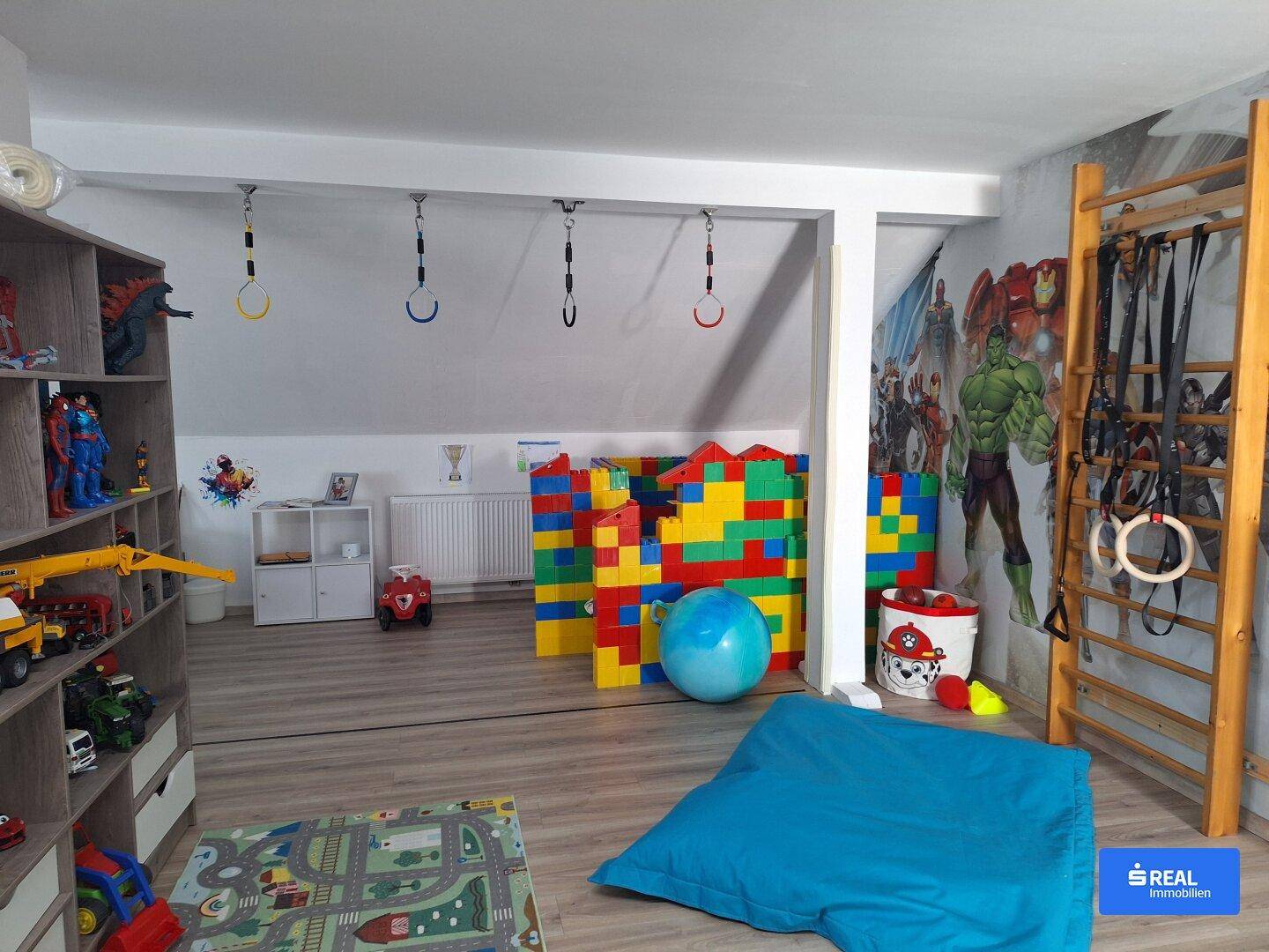 Großer Spielraum mit Kletterwand, Turnringen und bunten Bausteinen.