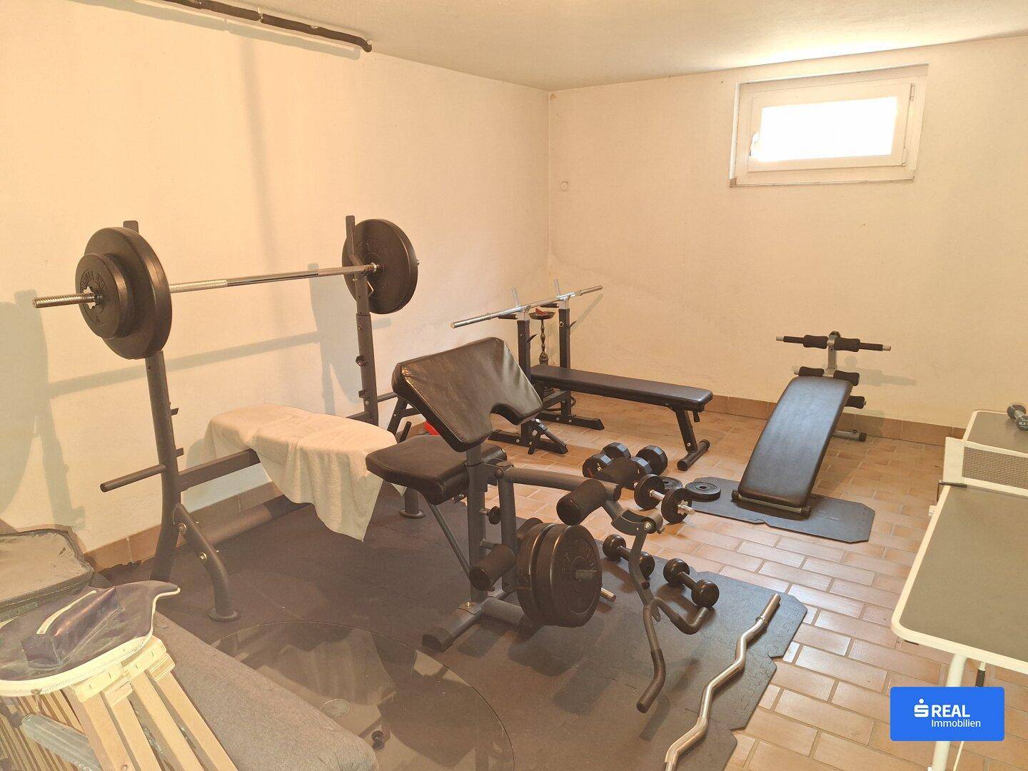 Fitnessraum im Keller mit verschiedenen Trainingsgeräten und Fliesenboden.