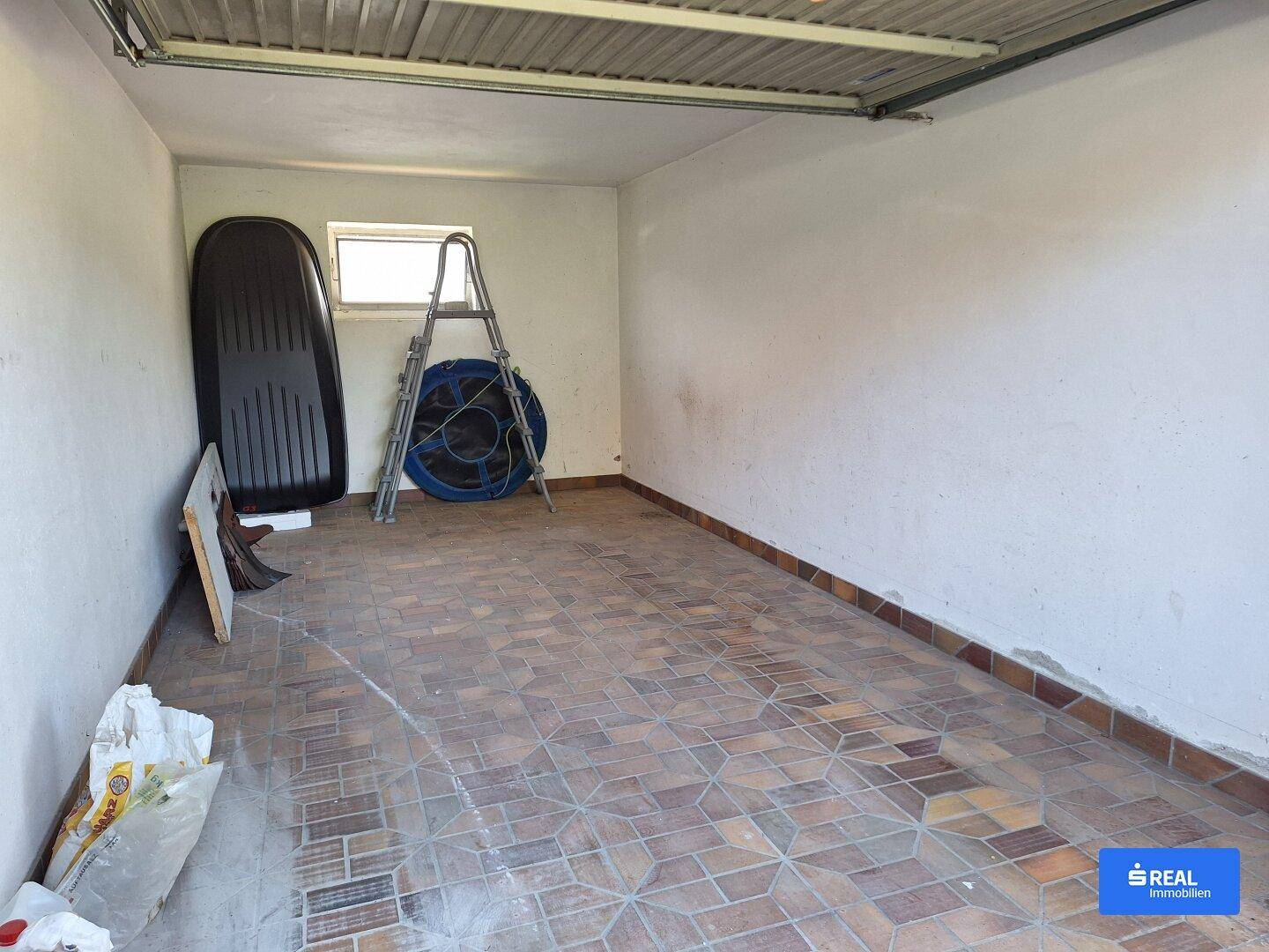 Geräumige Garage mit Fliesenboden und Stauraum für verschiedene Gegenstände.