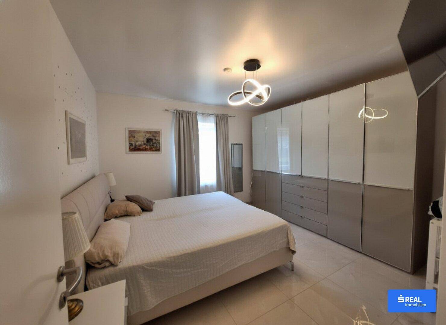 Schlafzimmer mit großem Doppelbett, Einbauschränken und modernem Deckenlicht.