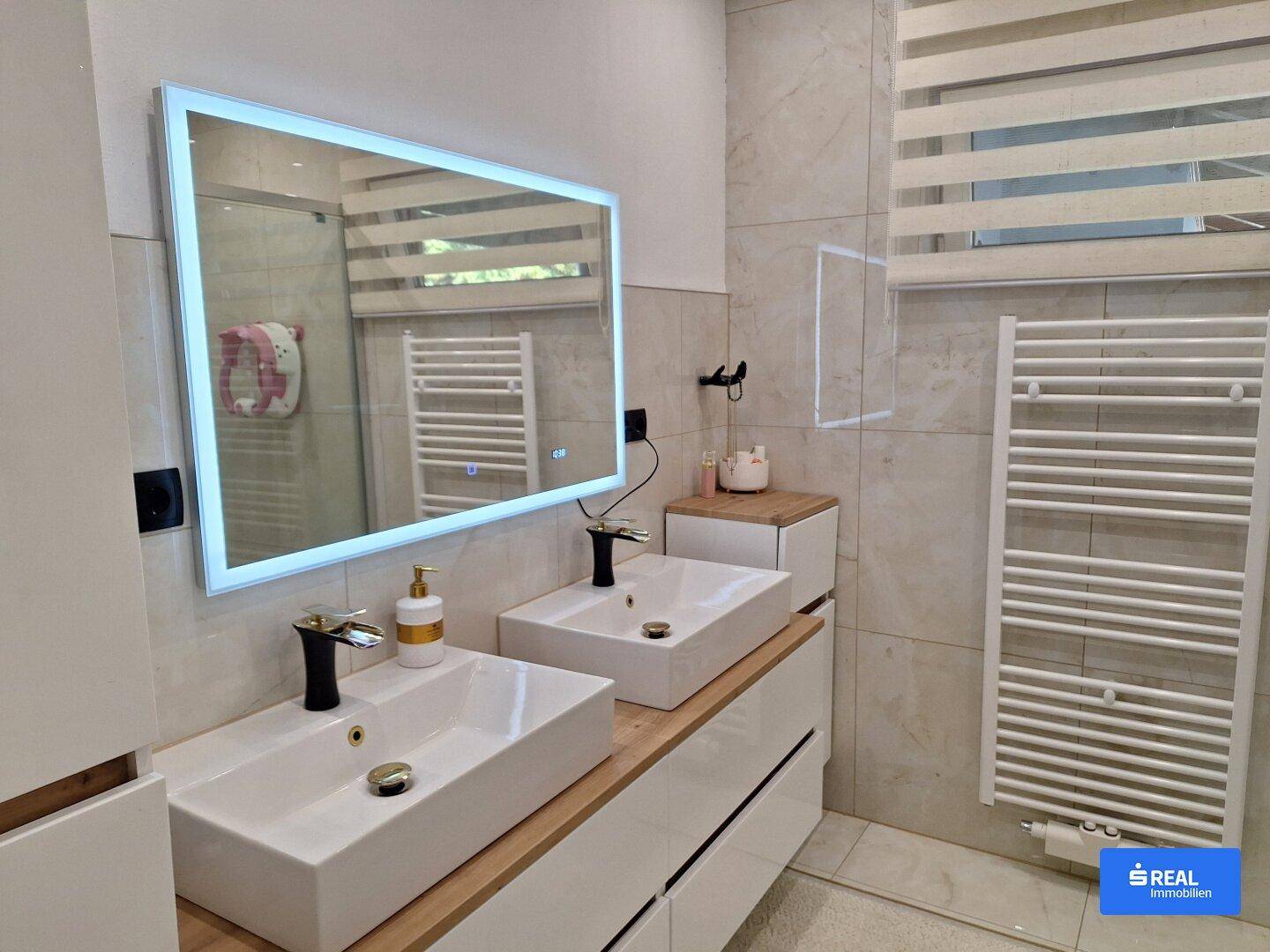 Modernes Badezimmer mit Doppelwaschbecken, beleuchtetem Spiegel und Handtuchheizkörper.