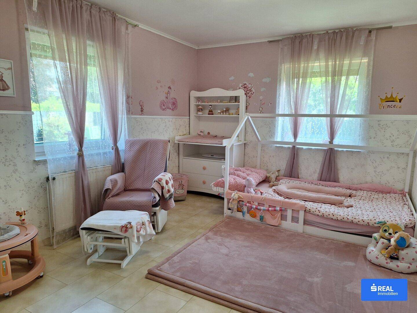 Helles Kinderzimmer in Rosa mit Hausbett, Wickelkommode und Schaukelstuhl, ideal für ein kleines Mädchen.