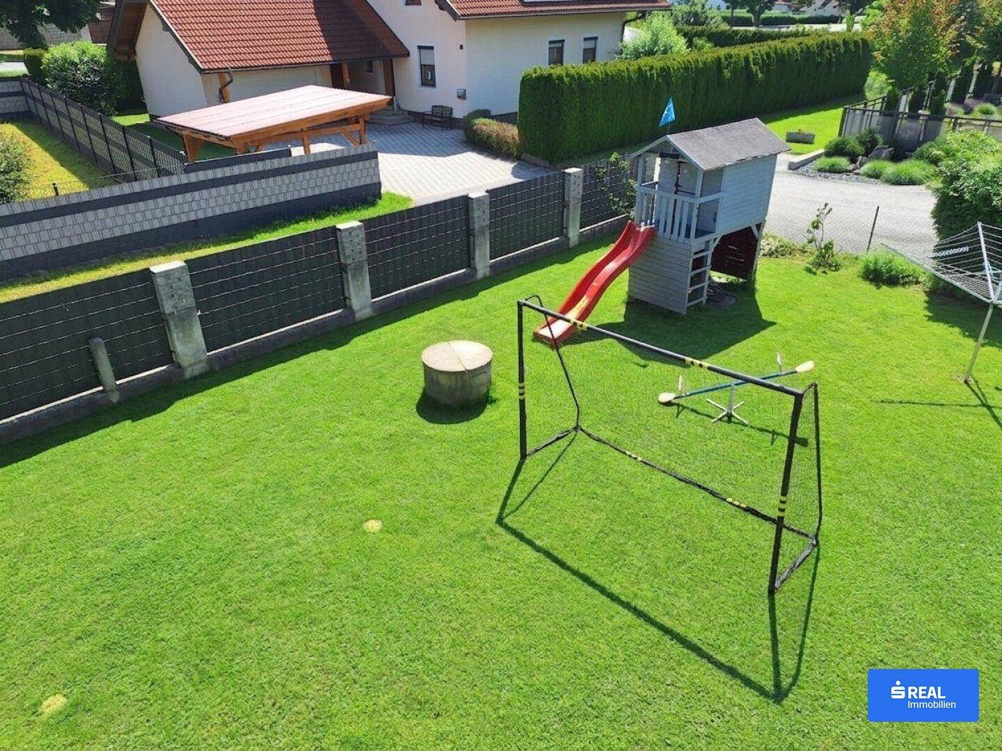 Großer, gepflegter Garten mit Spielhaus, Rutsche und Fußballtoren, umgeben von einem Zaun.