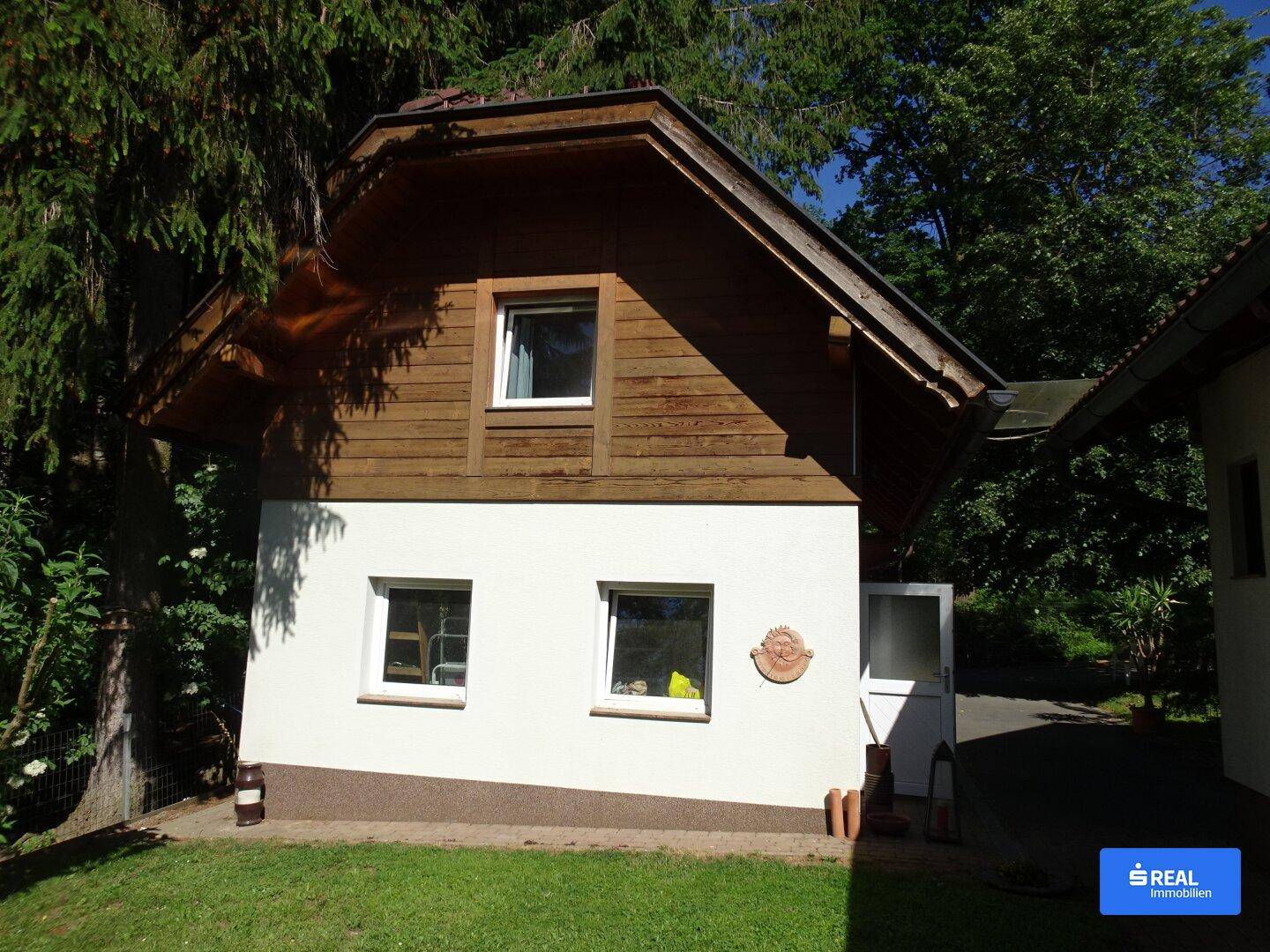 Charmantes Haus mit Holzfassade im oberen Bereich und weiß verputztem Erdgeschoss.