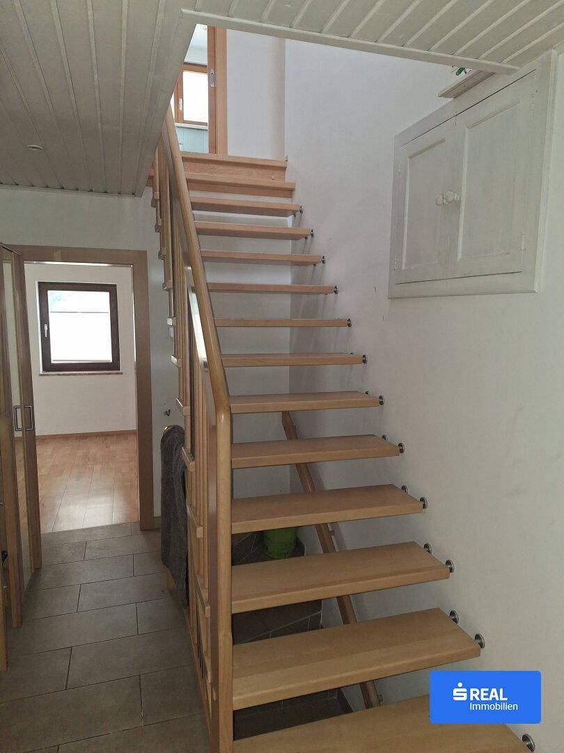 Heller Flur mit Holztreppe, die in die oberen Stockwerke führt, und Fliesenboden.
