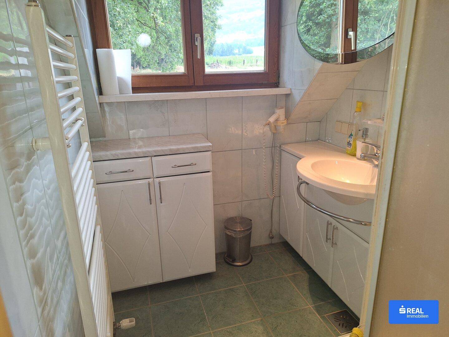 Badezimmer mit Waschbecken, Spiegelschrank und beheiztem Handtuchhalter, hell gefliest.