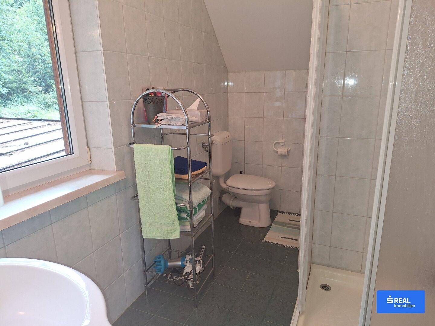 Kleines Badezimmer mit Dusche, WC und Fenster, ausgestattet mit hellen Fliesen.