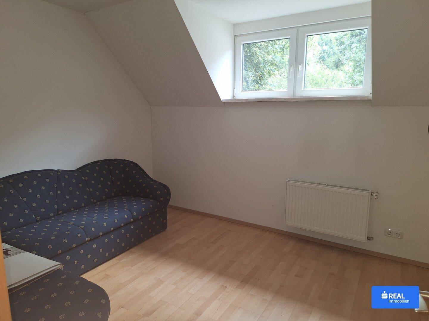 Helles Schlafzimmer mit Holzboden, Dachschräge und einem Fenster mit Blick ins Grüne.