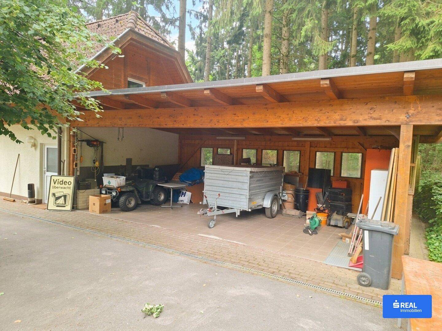 Geräumiger Carport mit Holzbalken, der als Abstellfläche für Fahrzeuge und Geräte dient.