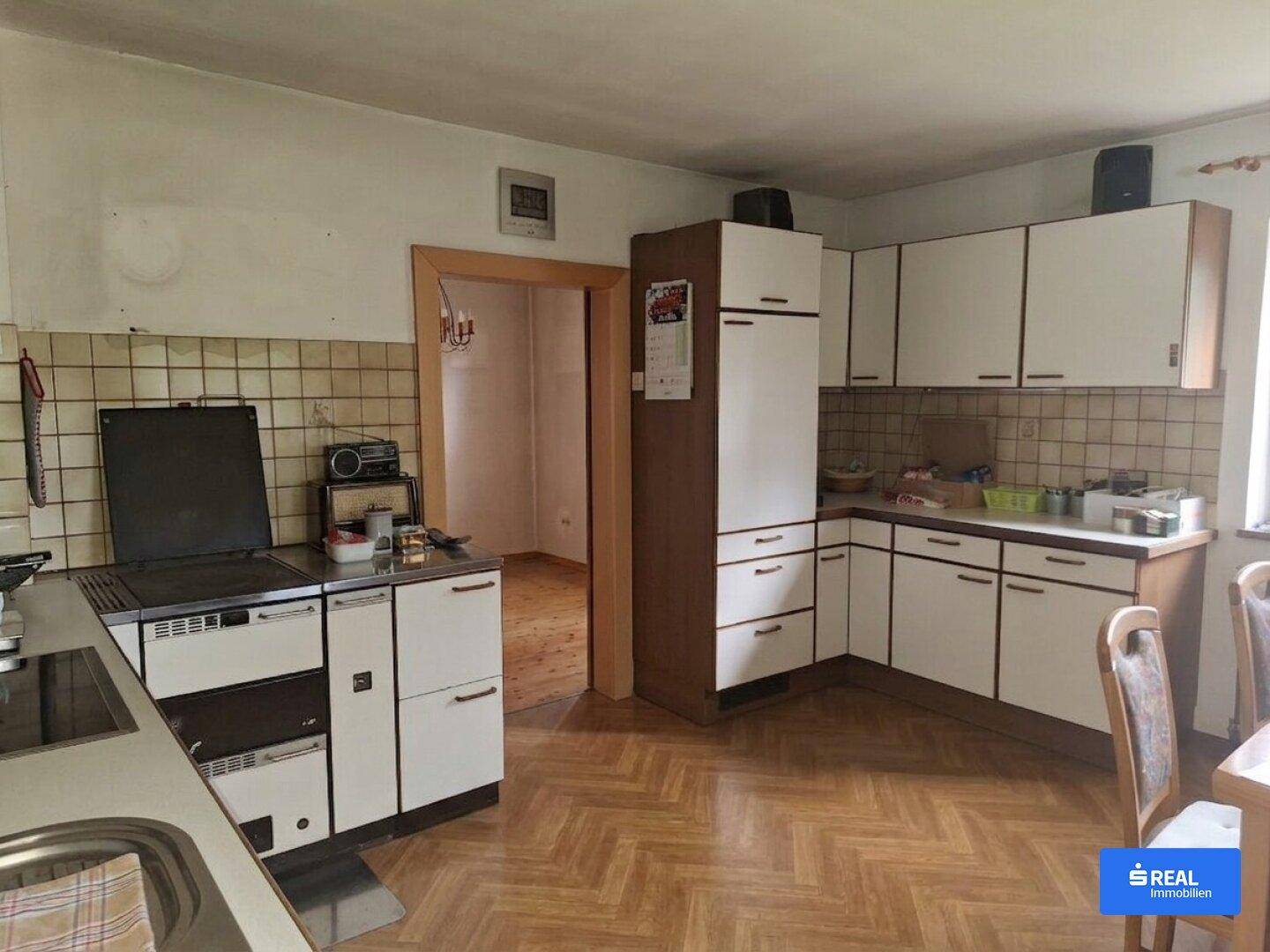 Traditionelle Küche mit Holzparkett, älteren Einbauschränken und einem klassischen Holzherd.