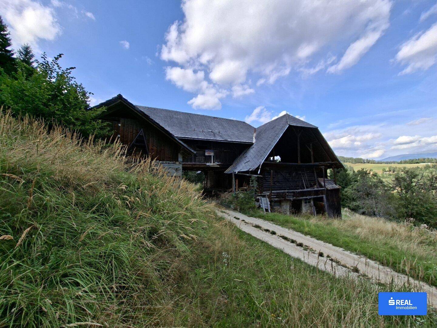 Altes, rustikales Holzgebäude auf einem Hügel mit Blick auf die umliegende Landschaft und Berge.