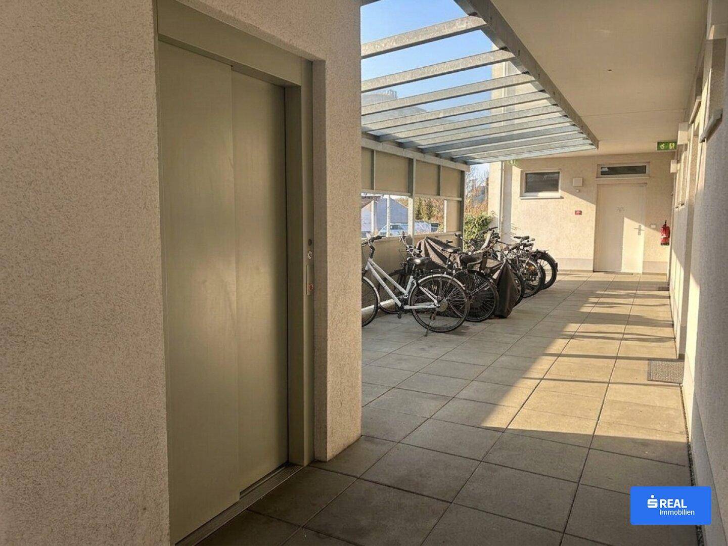 Überdachter Eingangsbereich mit Aufzug und Fahrradabstellmöglichkeiten für Bewohner.