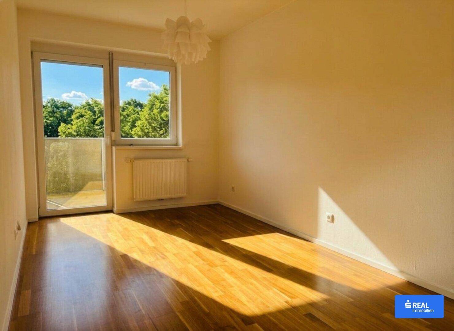 Geräumiges Zimmer mit Holzboden und großem Fenster, das viel Tageslicht hereinlässt.