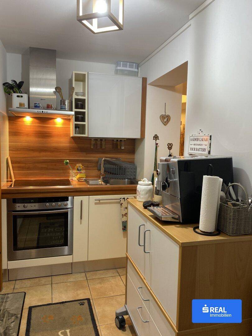 Kleine, funktionale Küchenzeile mit Backofen, Dunstabzugshaube und Kaffeemaschine.
