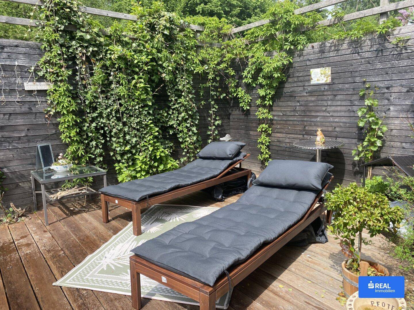 Sonnige Holzterrasse mit Liegestühlen und grüner Bepflanzung für entspannte Stunden.