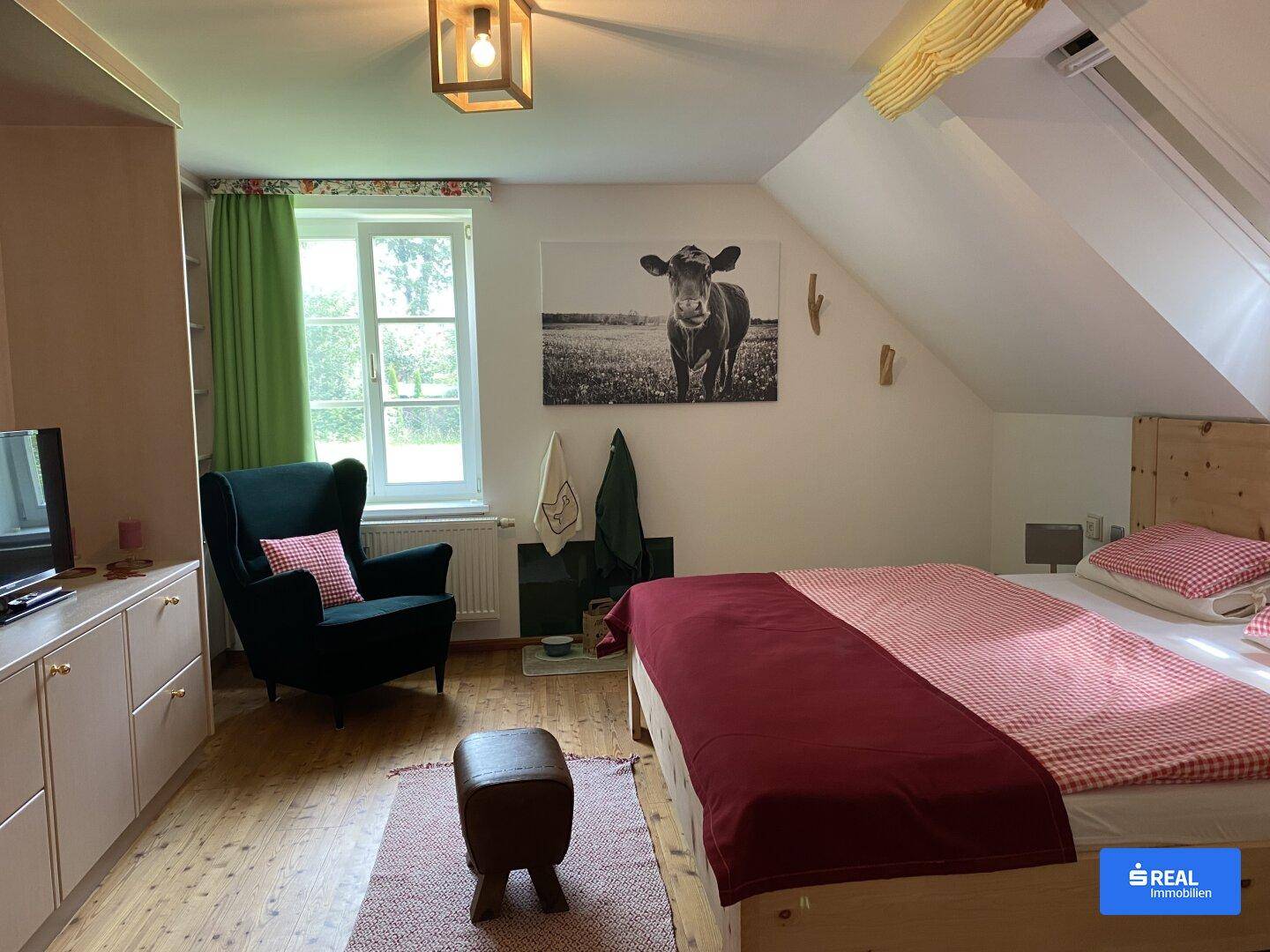 Gemütliches Schlafzimmer im Dachgeschoss mit Holzboden, Schrägdecke und Blick ins Grüne.