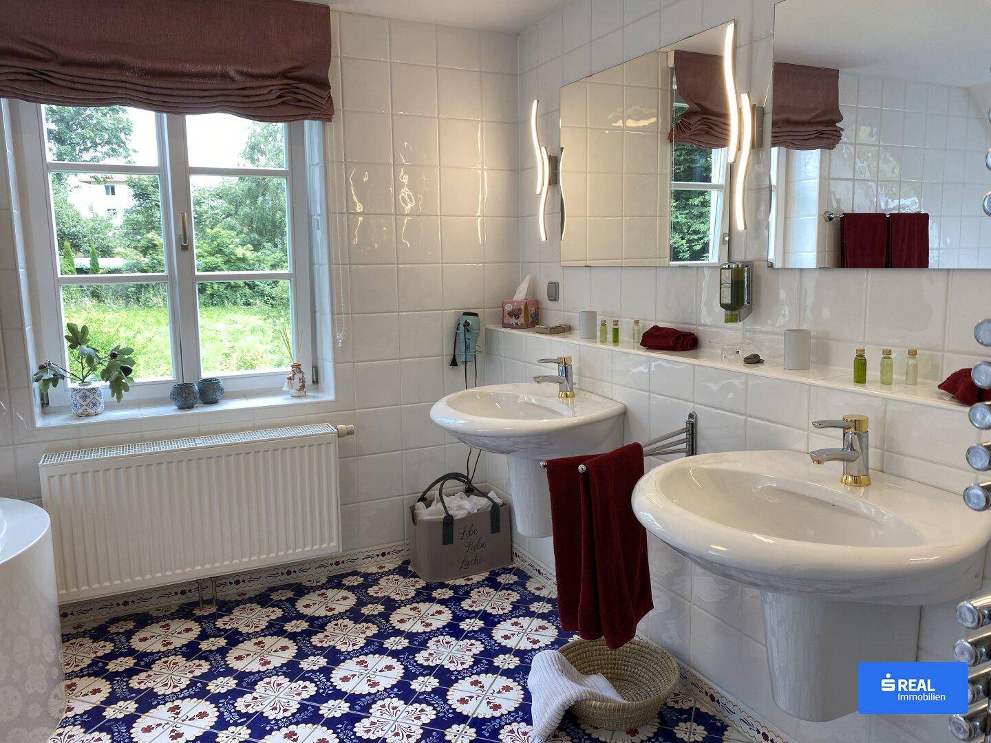 Helles Badezimmer mit Doppelwaschbecken, Fenster und auffälligem Fliesenbodenmuster.