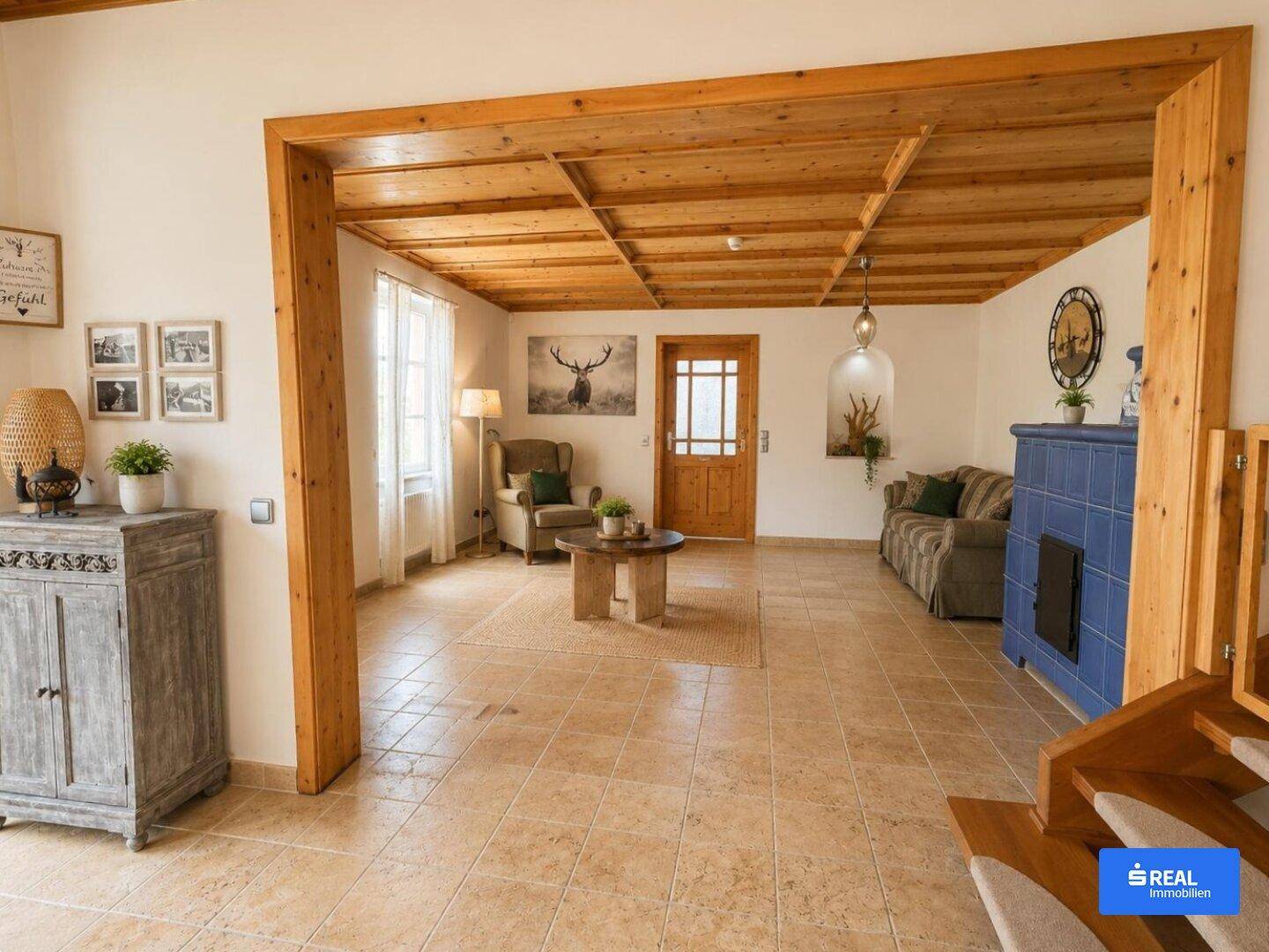 Offener Wohnbereich mit Holzbalkendecke, Fliesenboden und traditionellem Kachelofen.