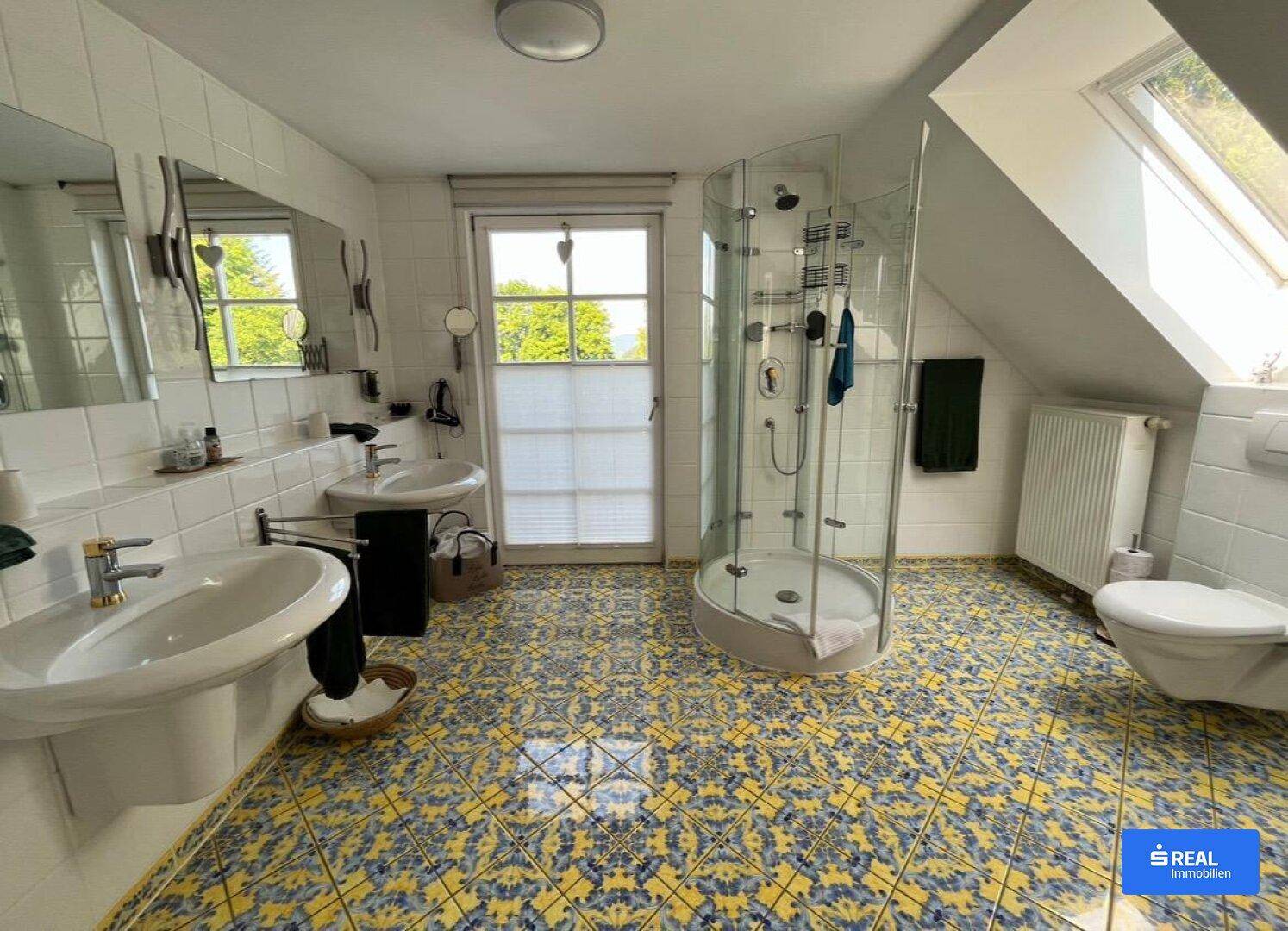 Geräumiges Badezimmer im Dachgeschoss mit Dusche, Doppelwaschbecken und farbenfrohem Fliesenboden.