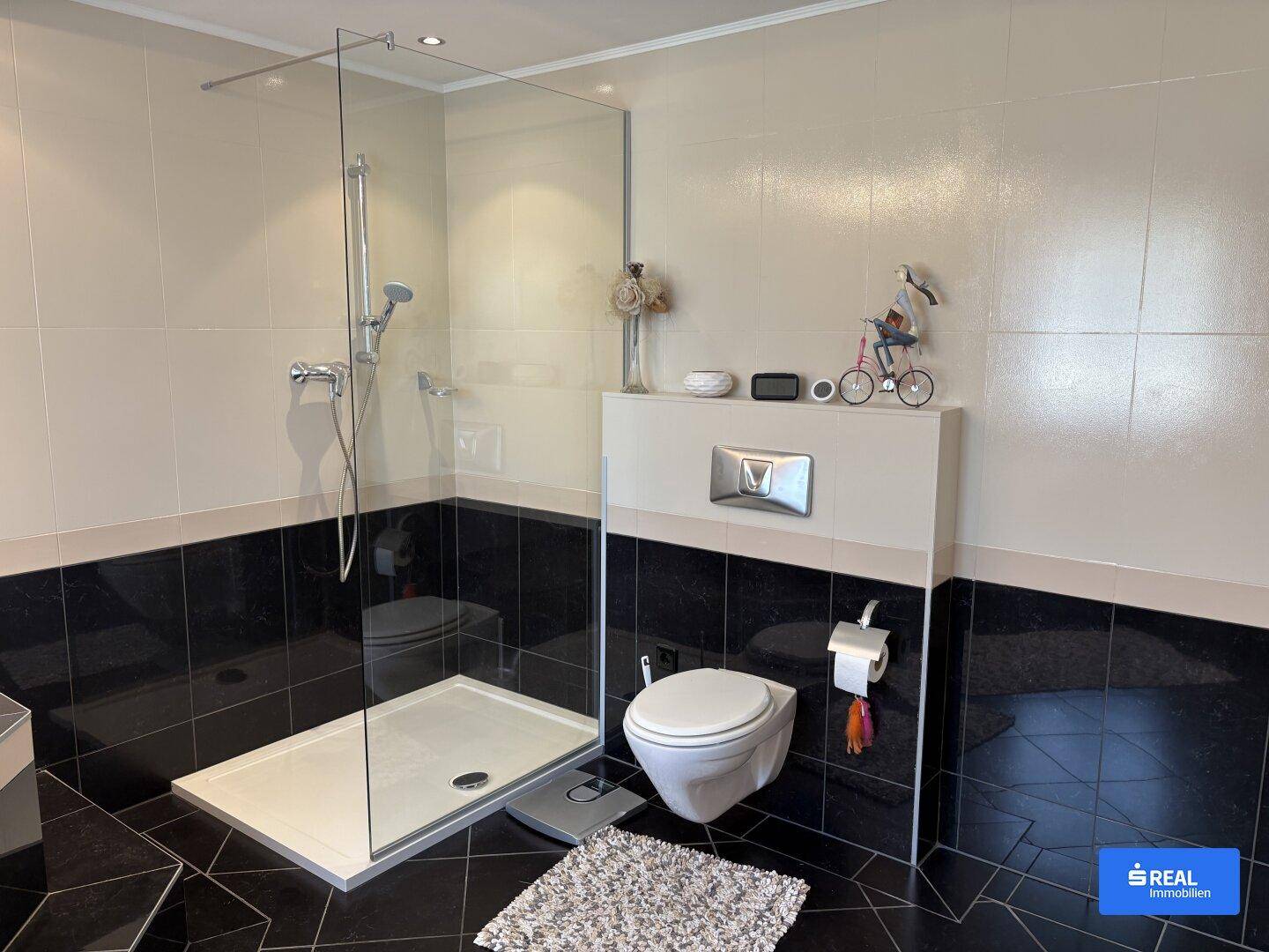 Badezimmer mit ebenerdiger Dusche, wandhängendem WC und schwarzen Bodenfliesen.