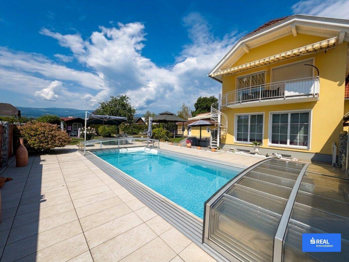Weitläufiger Gartenbereich mit großem Swimmingpool und gelbem Wohnhaus unter blauem Himmel.