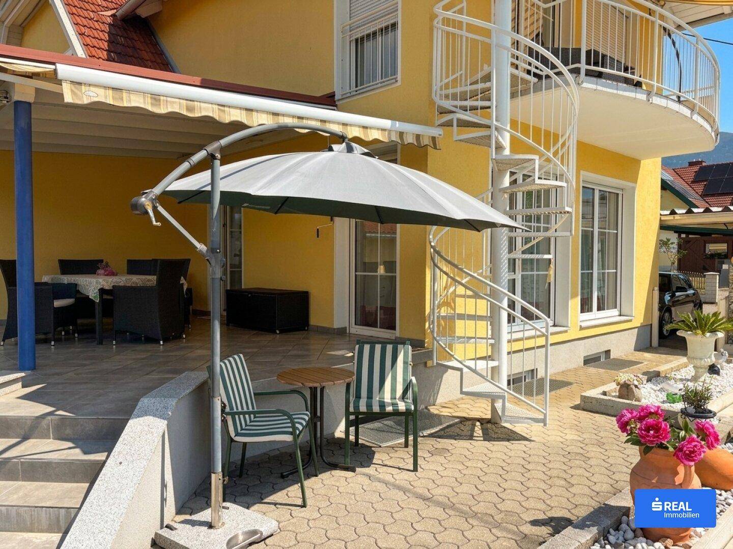 Gemütliche Terrasse mit Sonnenschirm und Sitzgelegenheiten neben einer eleganten Wendeltreppe.