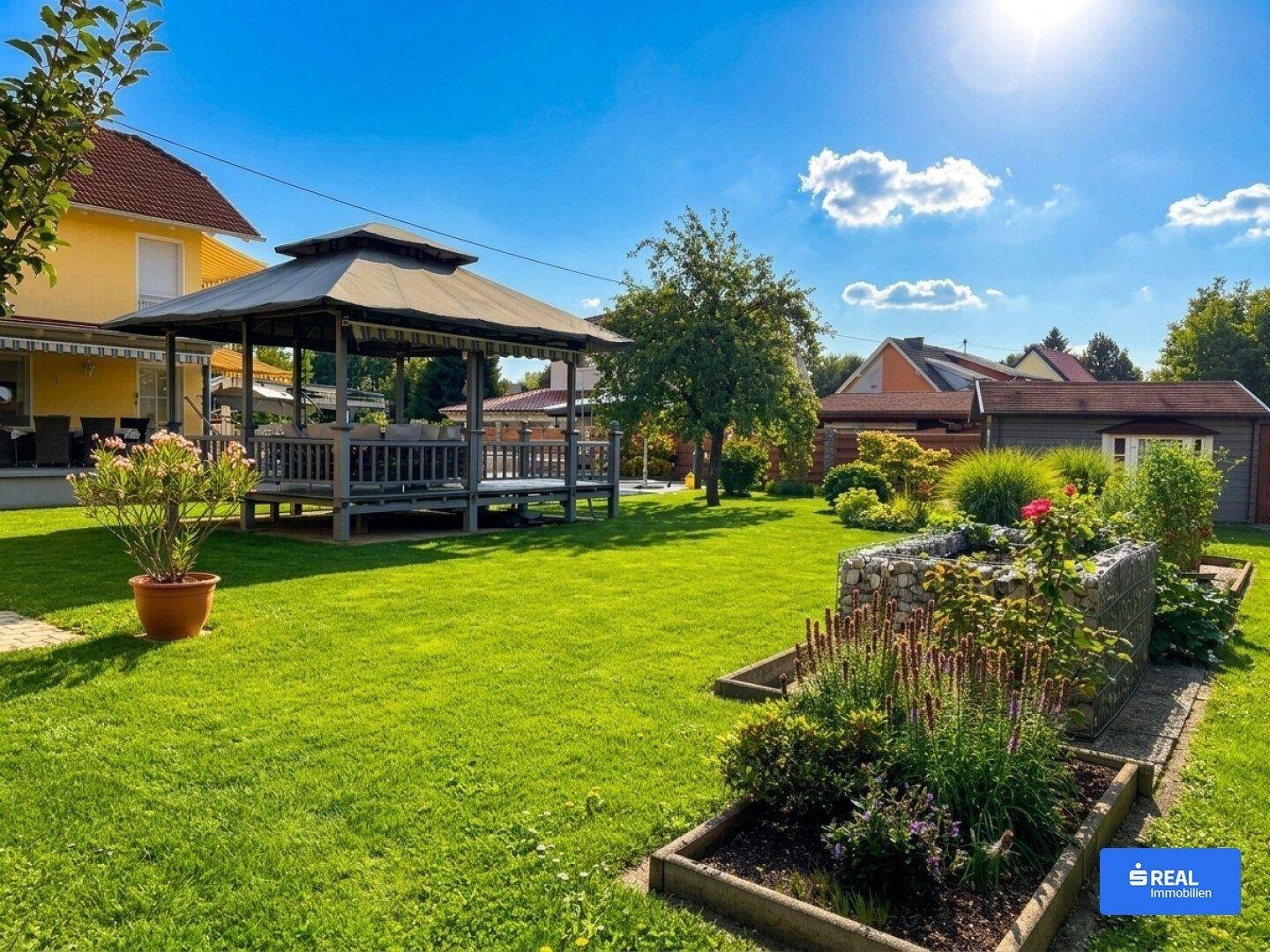 Großer, sonniger Garten mit Rasenfläche, Gartenlaube und Blumenbeeten unter blauem Himmel.