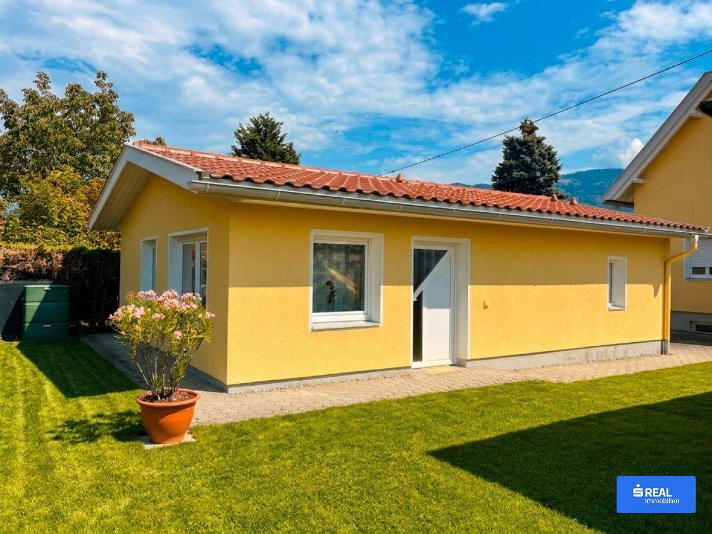 Kleines gelbes Nebengebäude im Garten mit Rasenfläche und blühenden Pflanzen.
