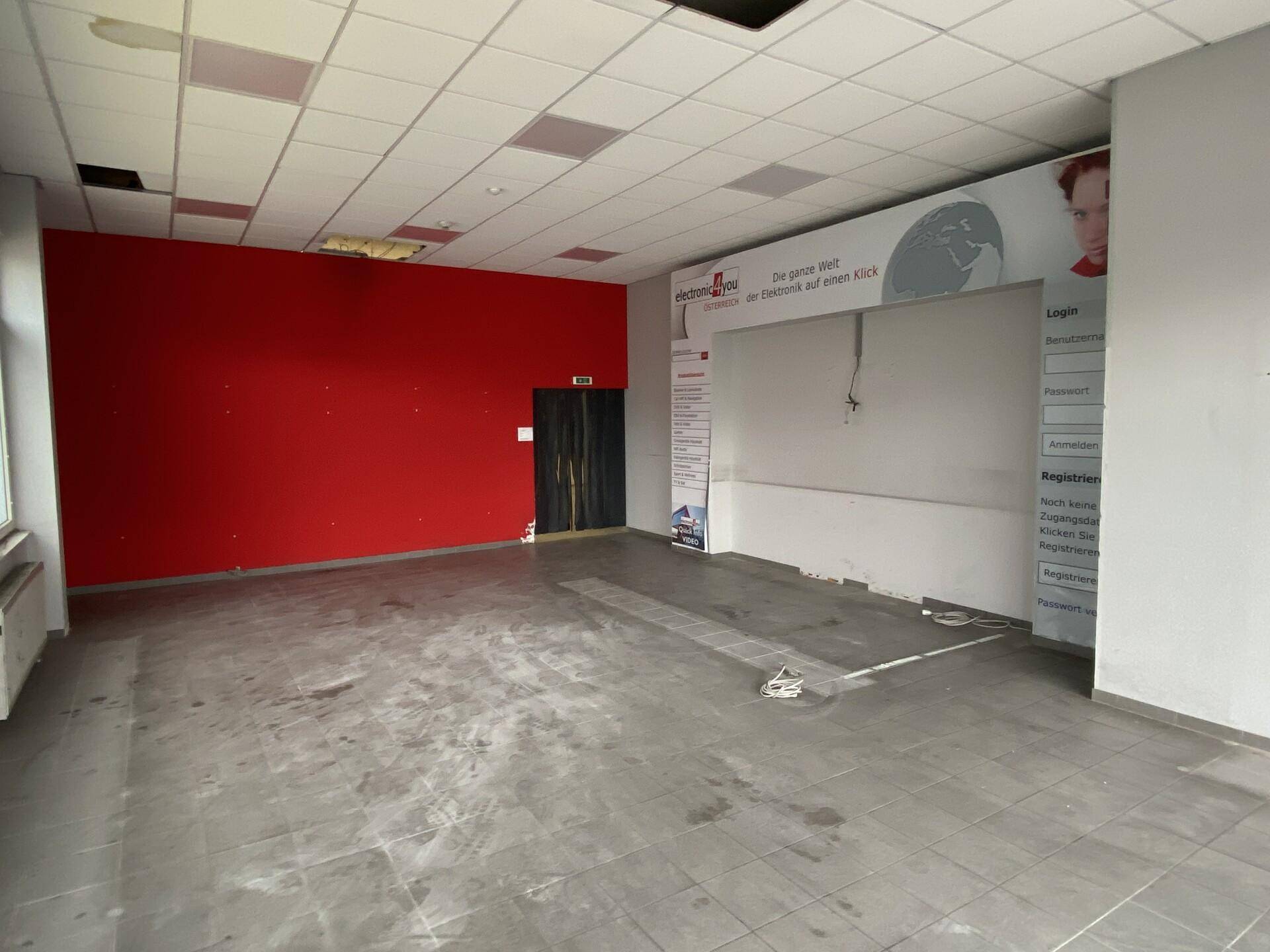 Geräumiger Ladenbereich mit roter Akzentwand, Fliesenboden und abgehängter Decke, bereit zur Gestaltung.