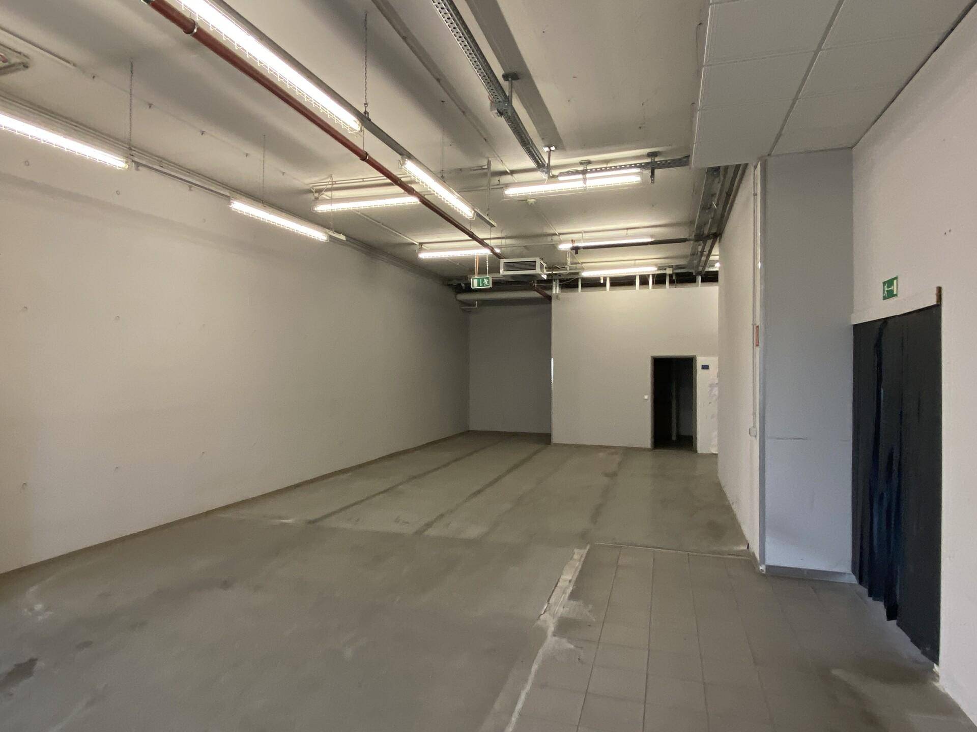 Großer Lagerraum mit Betonboden, sichtbaren Installationen und effizienter Deckenbeleuchtung.